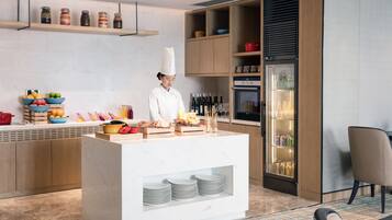 A modern kitchen with a chef, a fruit bowl, a wine rack, and a refrigerator.