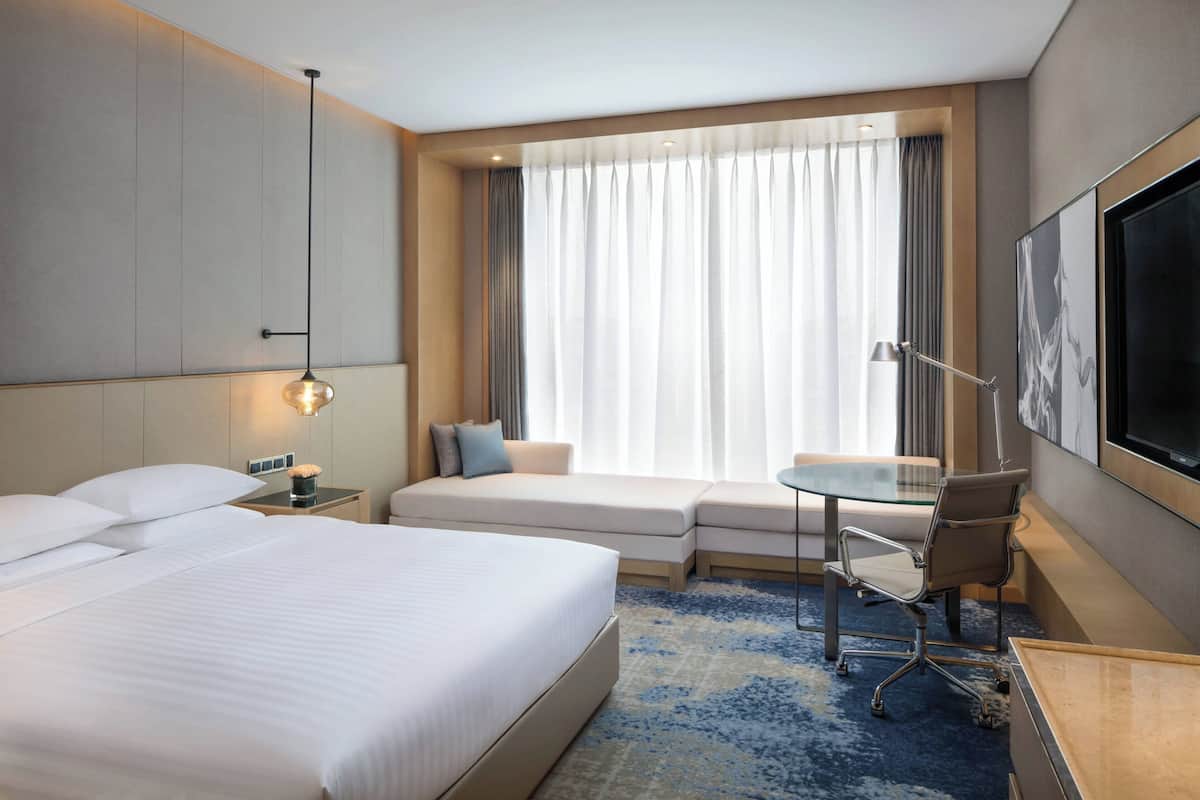Une chambre d’hôtel avec un grand lit, un bureau avec une chaise, une télévision et une fenêtre avec des rideaux.
