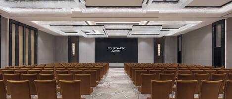 A conference room with rows of chairs, a large screen displaying 'Courtyard Marriott', and a patterned carpet.