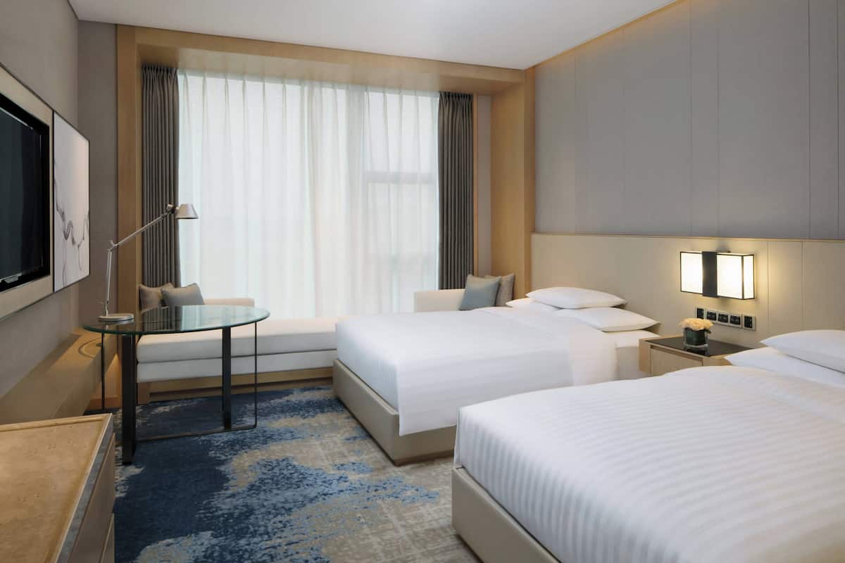 Une chambre d’hôtel avec deux lits, un bureau, une télévision et une fenêtre avec des rideaux.