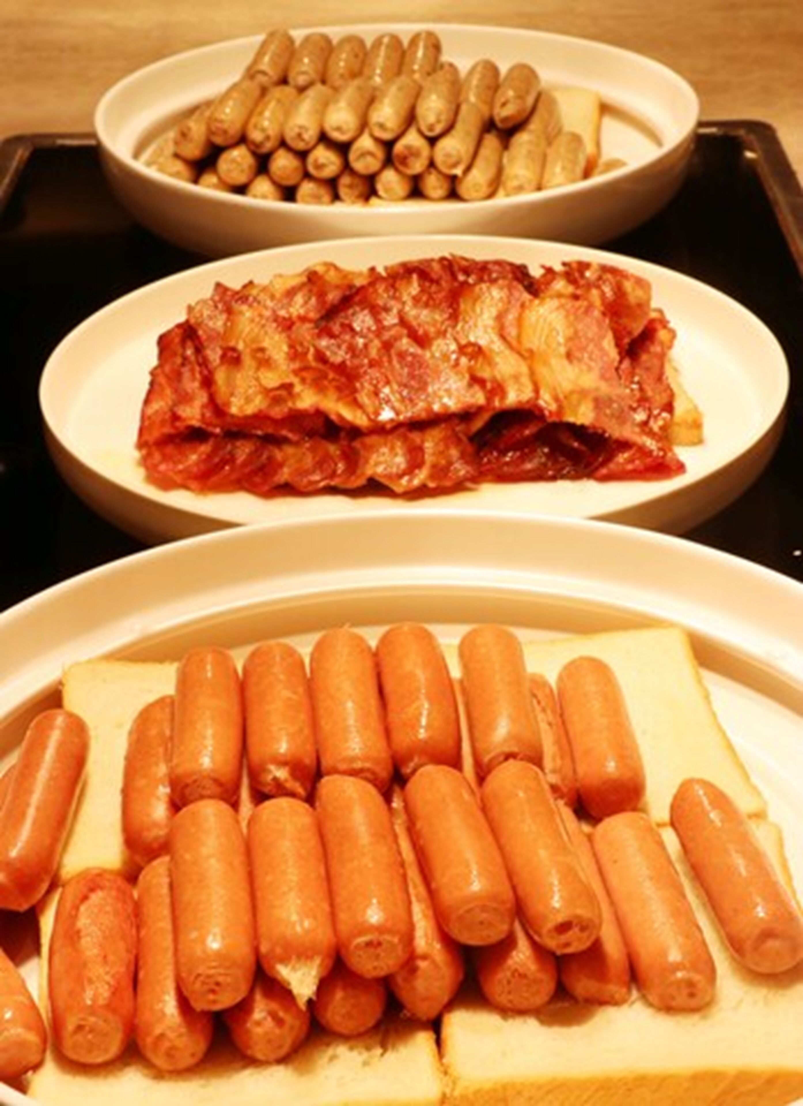 Three plates of food: sausages, a meat dish, and a meat dish with bread.