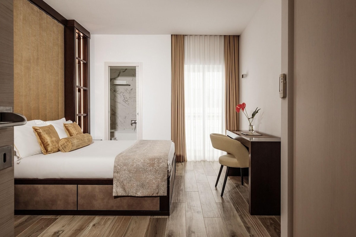 A hotel room with a bed, a desk, a chair, a wardrobe, and a bathroom door.