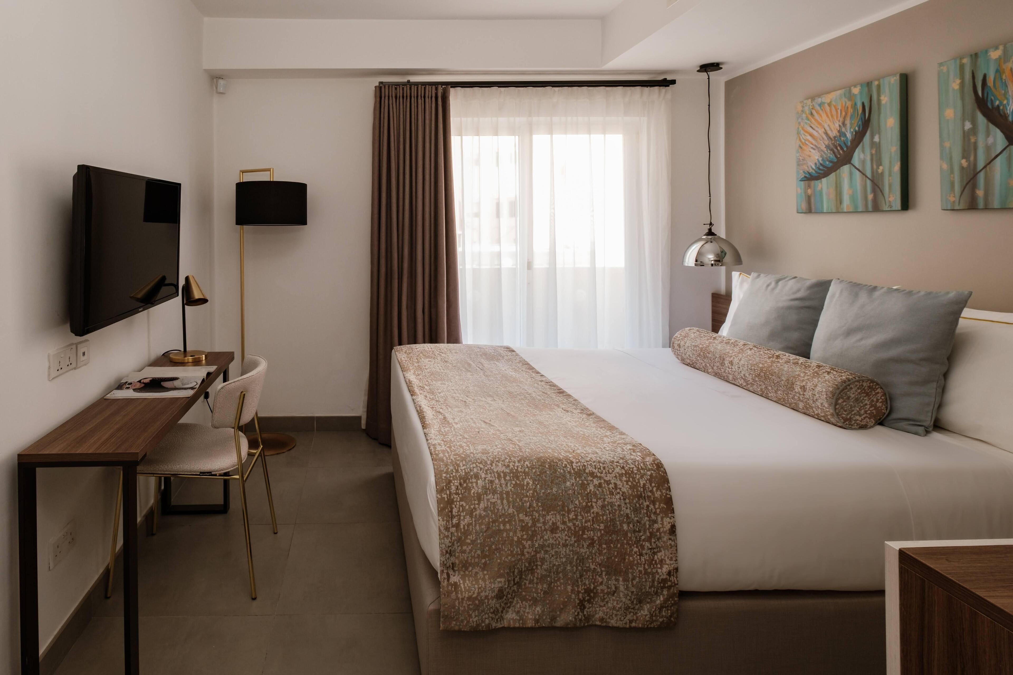 Habitación de hotel con cama, escritorio, silla, televisión y obra de arte en la pared.