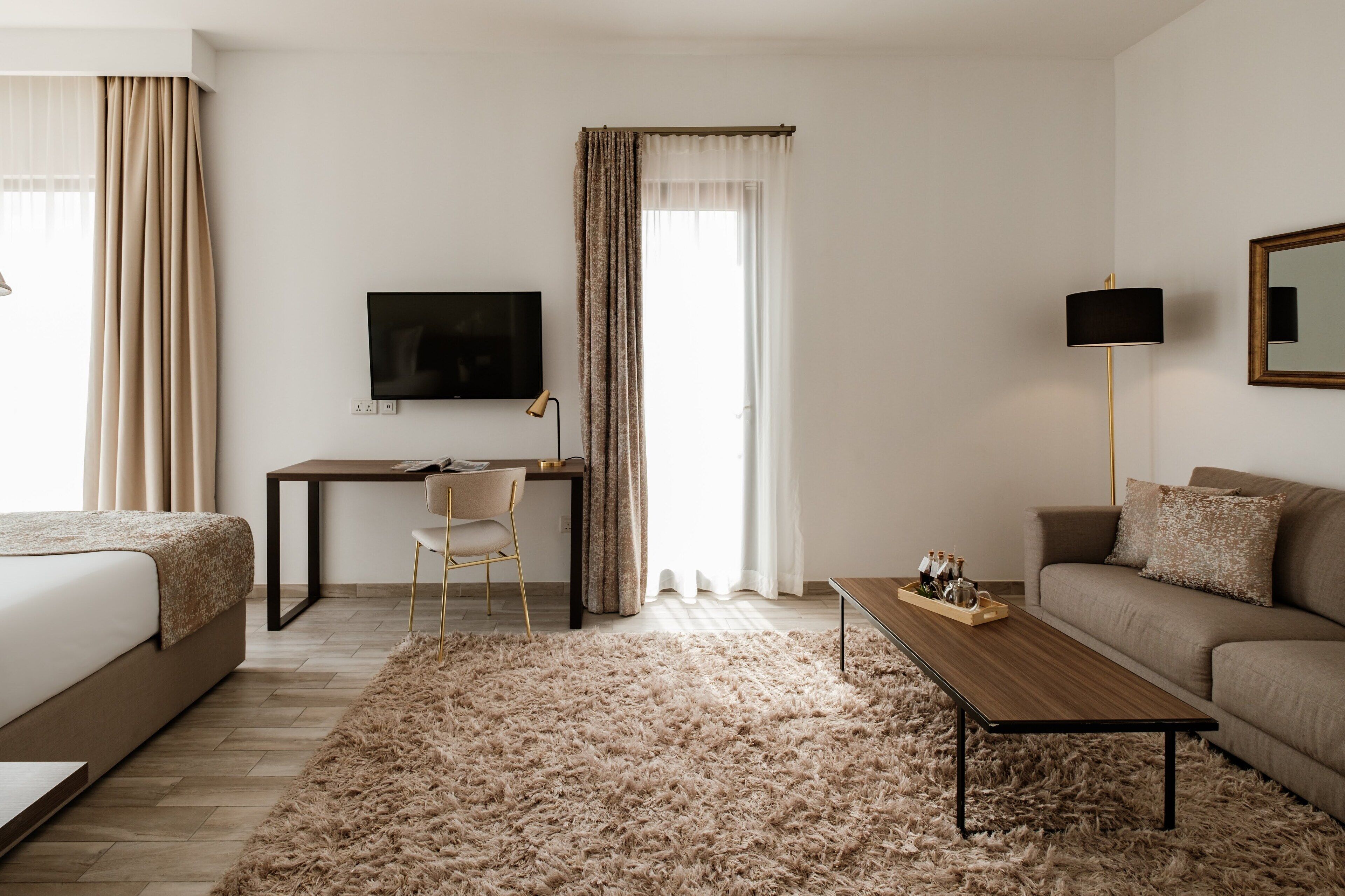 Ein modernes Hotelzimmer mit Bett, Schreibtisch mit Stuhl, Sofa, Fernseher und Couchtisch.
