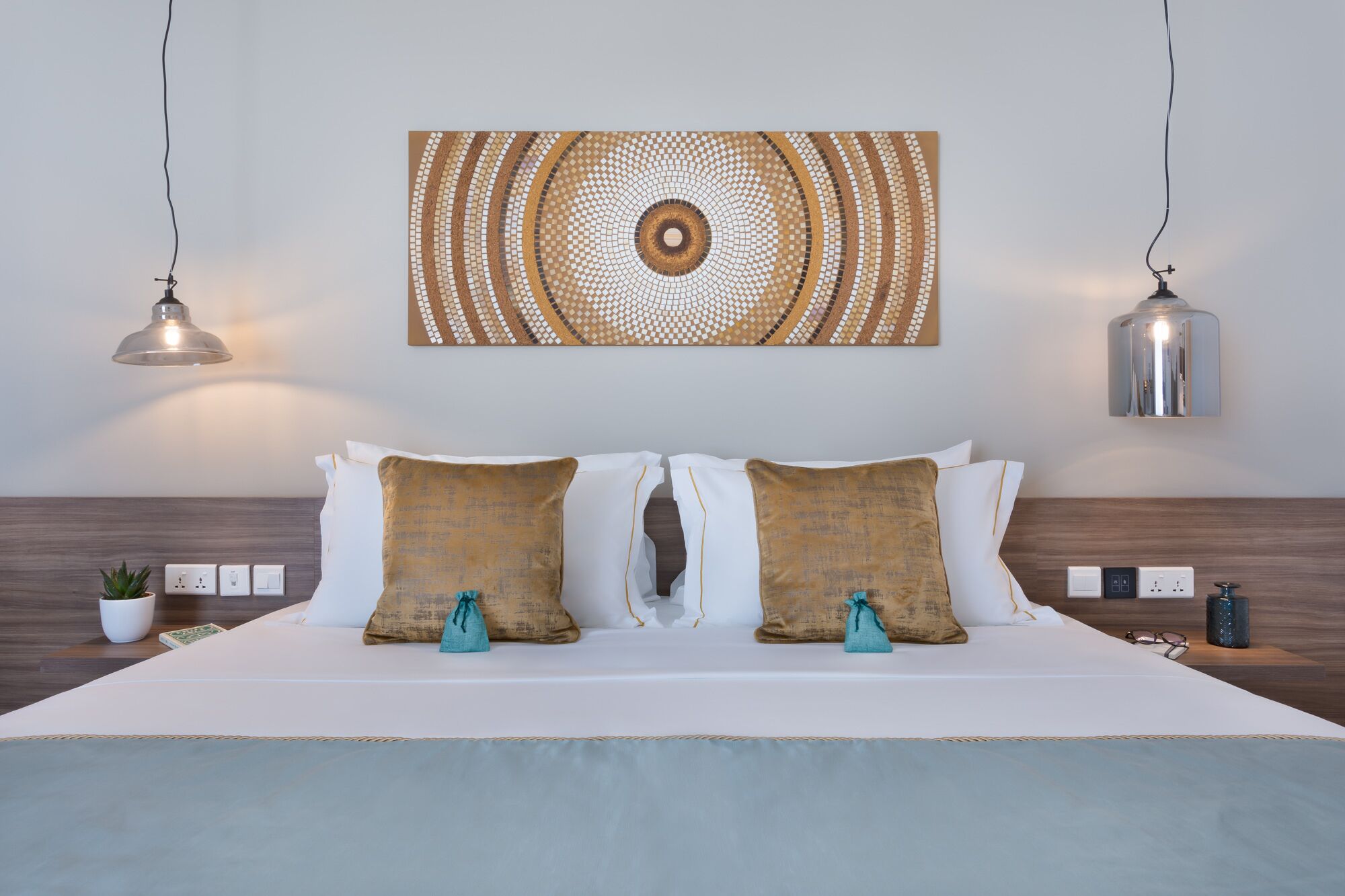 A neatly made bed with two pillows, a wall-mounted artwork, and two pendant lights.