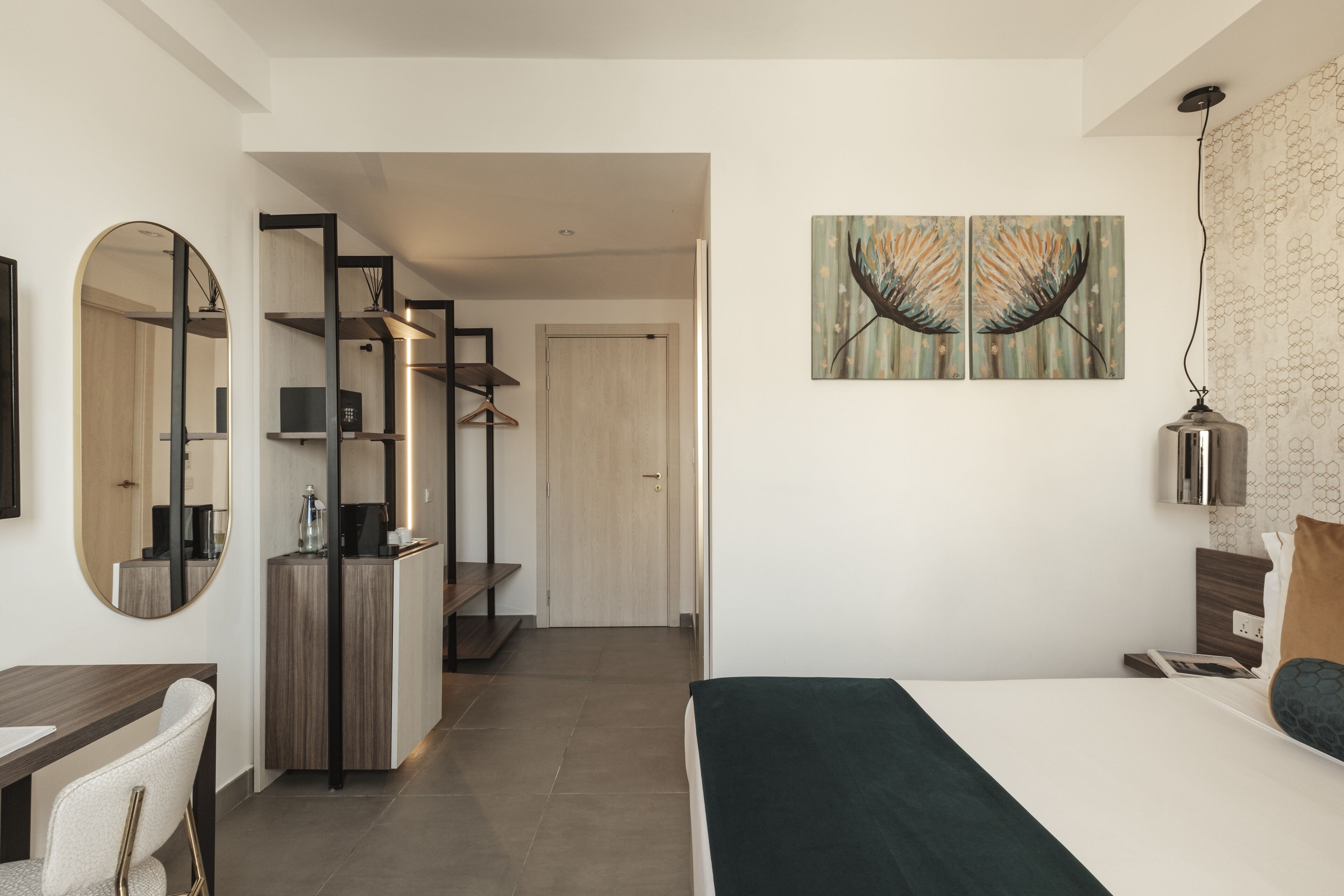 A modern bedroom with a bed, a desk, and a mirror. There is a door leading to another room.