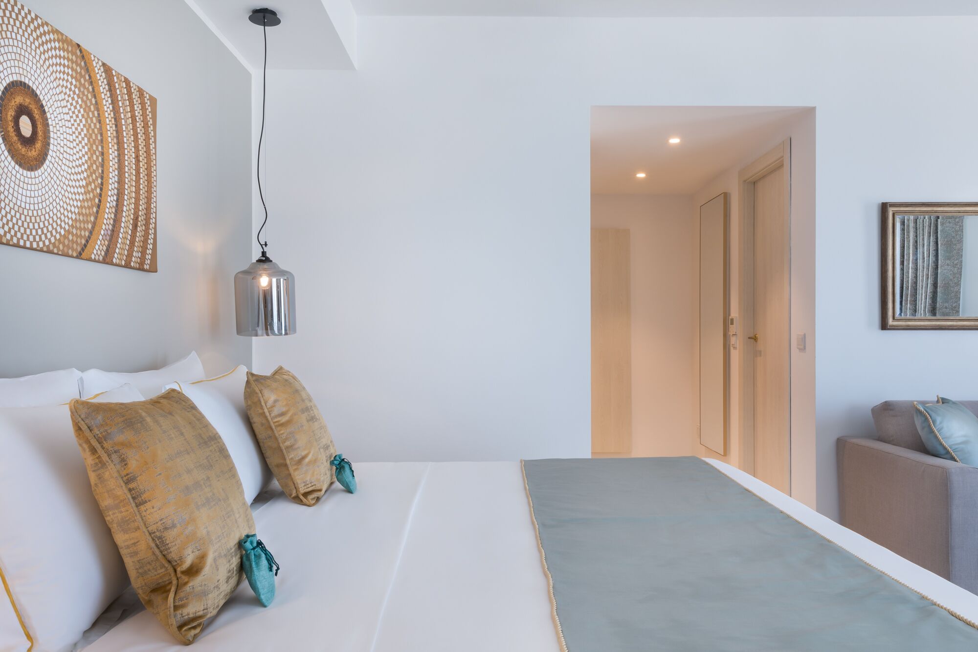 A modern bedroom with a large bed, a hanging light fixture, and a view into an adjacent room.