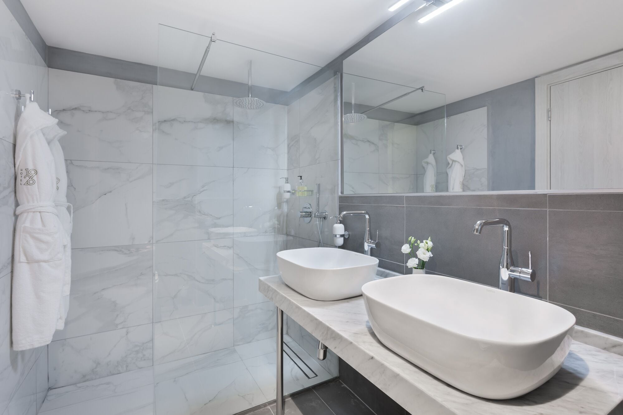 Un bagno moderno con due lavandini, una cabina doccia in vetro e uno specchio grande.