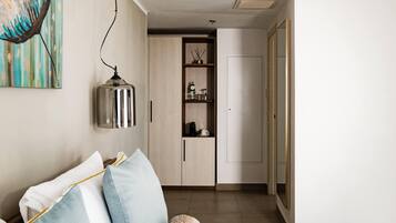 Uma sala de estar moderna com um sofá, uma mesa de centro e um quadro na parede. Cozinha visível através de uma porta aberta, com armários e bancada.