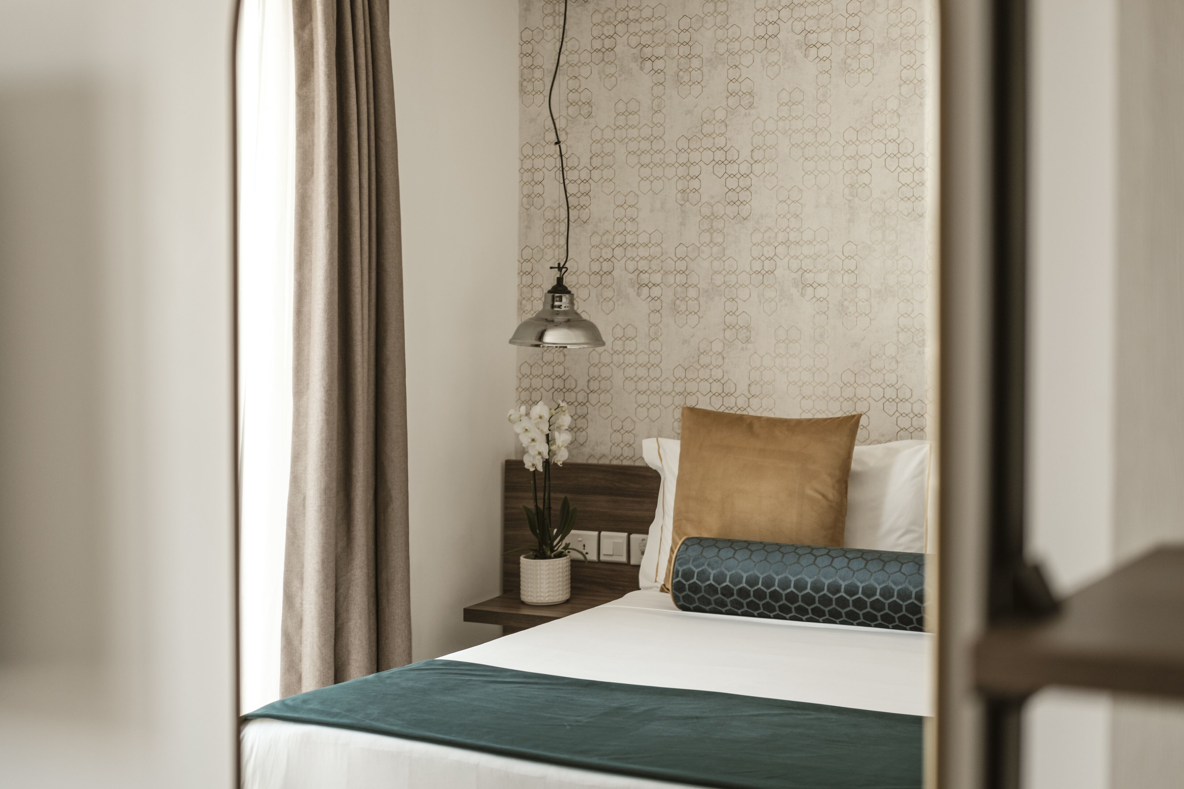 A neatly made bed with a white and teal bedspread, a wooden headboard, and a bedside table with a potted orchid.