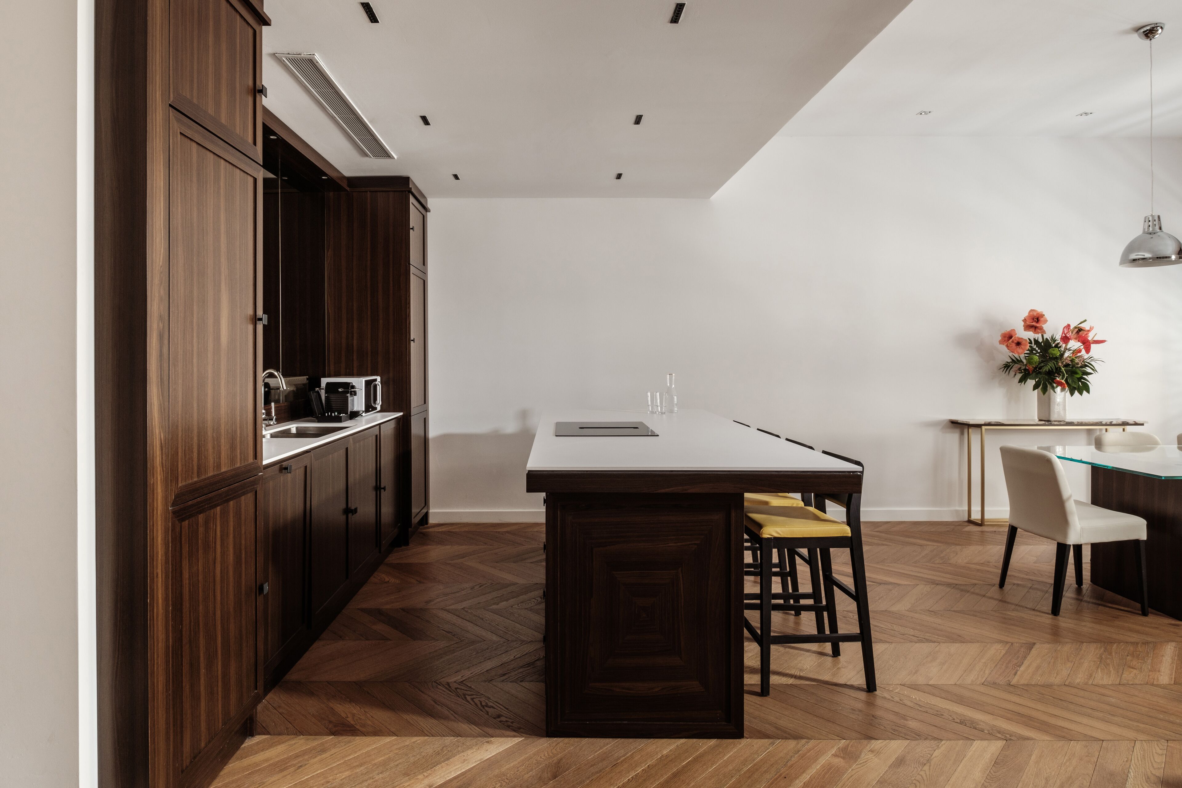 A modern kitchen with wooden cabinets, a central island, and a dining area with chairs.