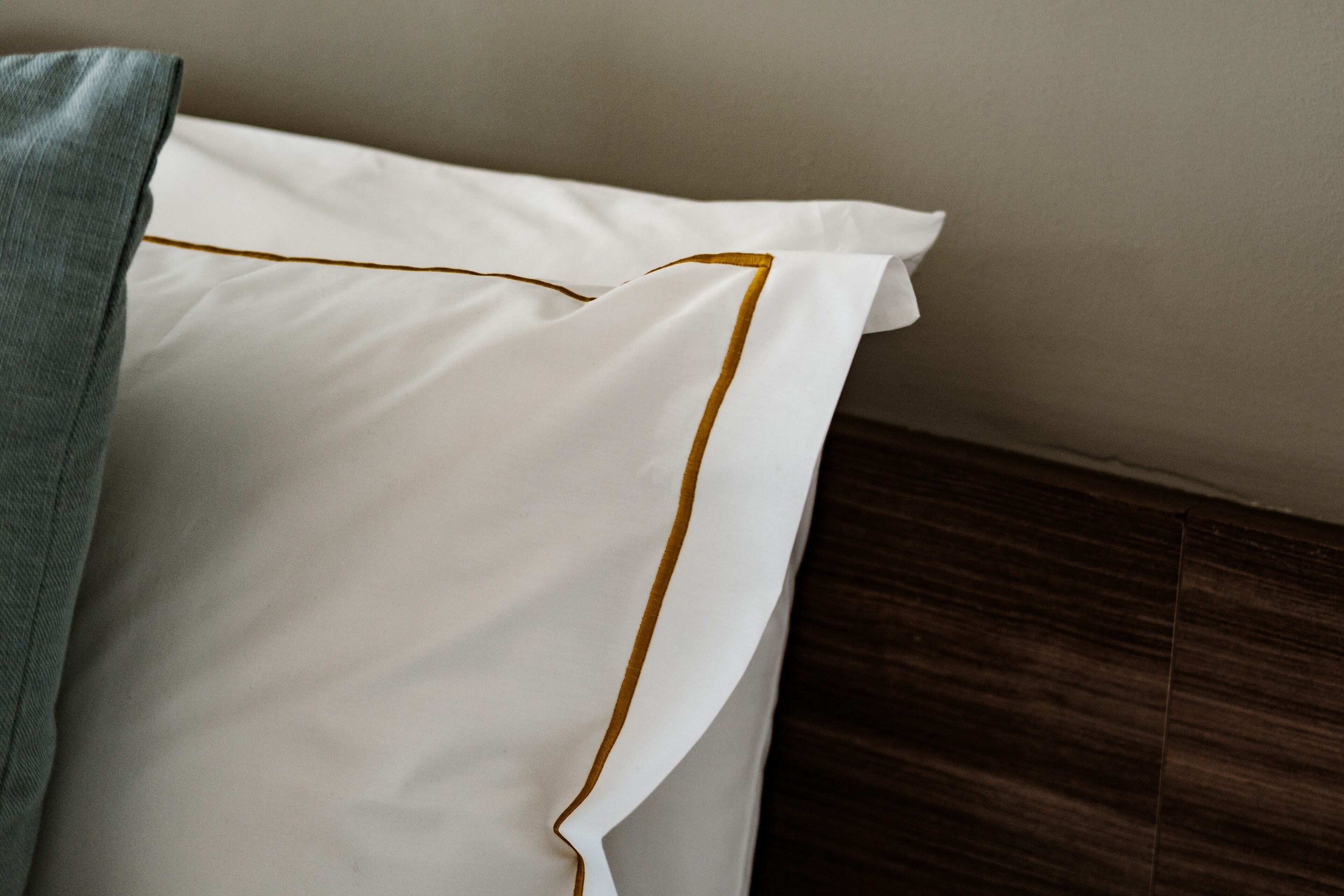 Almohada blanca con detalle dorado sobre piso de madera.