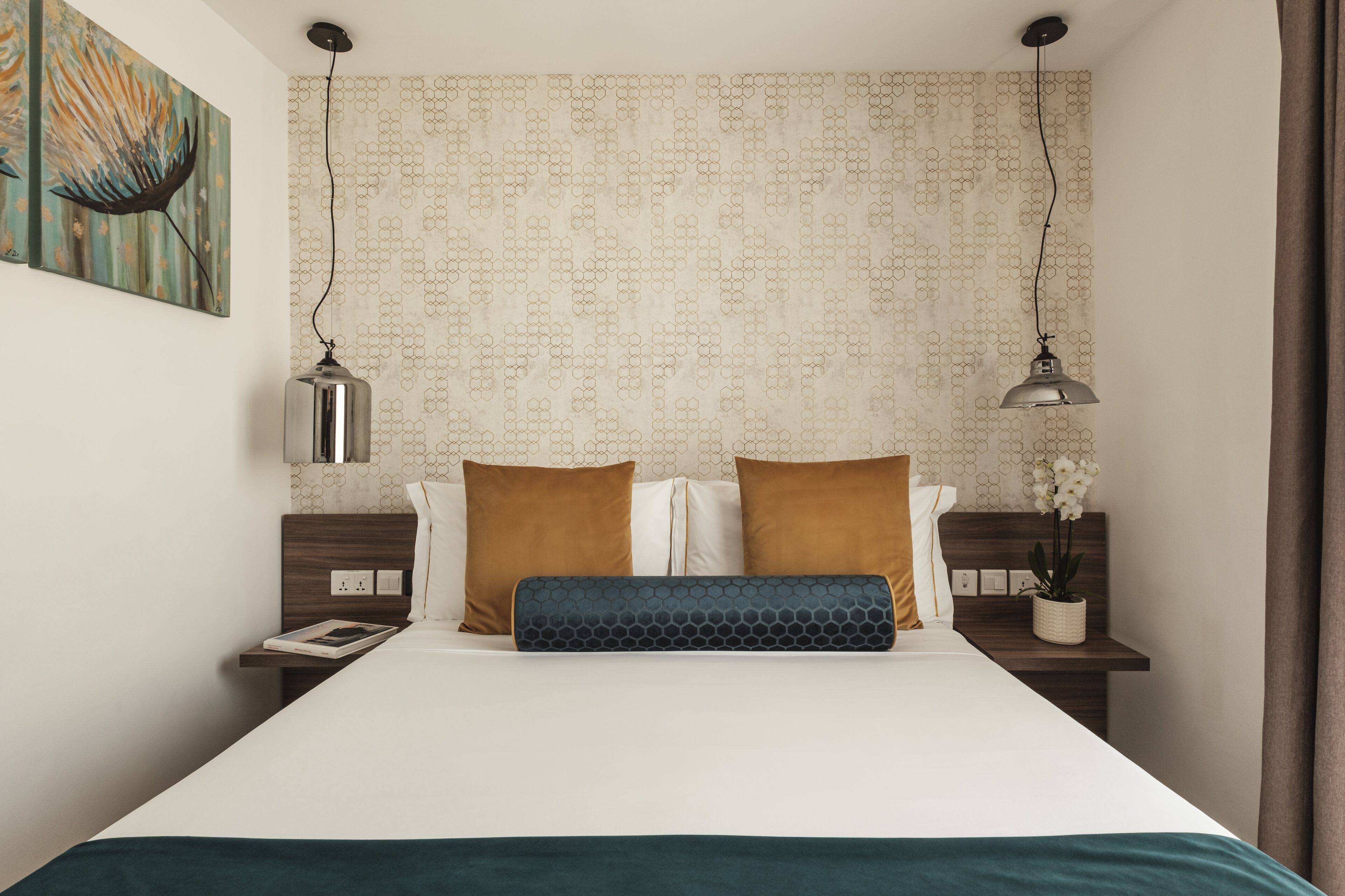 Een netjes ingerichte hotelkamer met een bed, twee nachtkastjes, een wandlamp en een potplant.