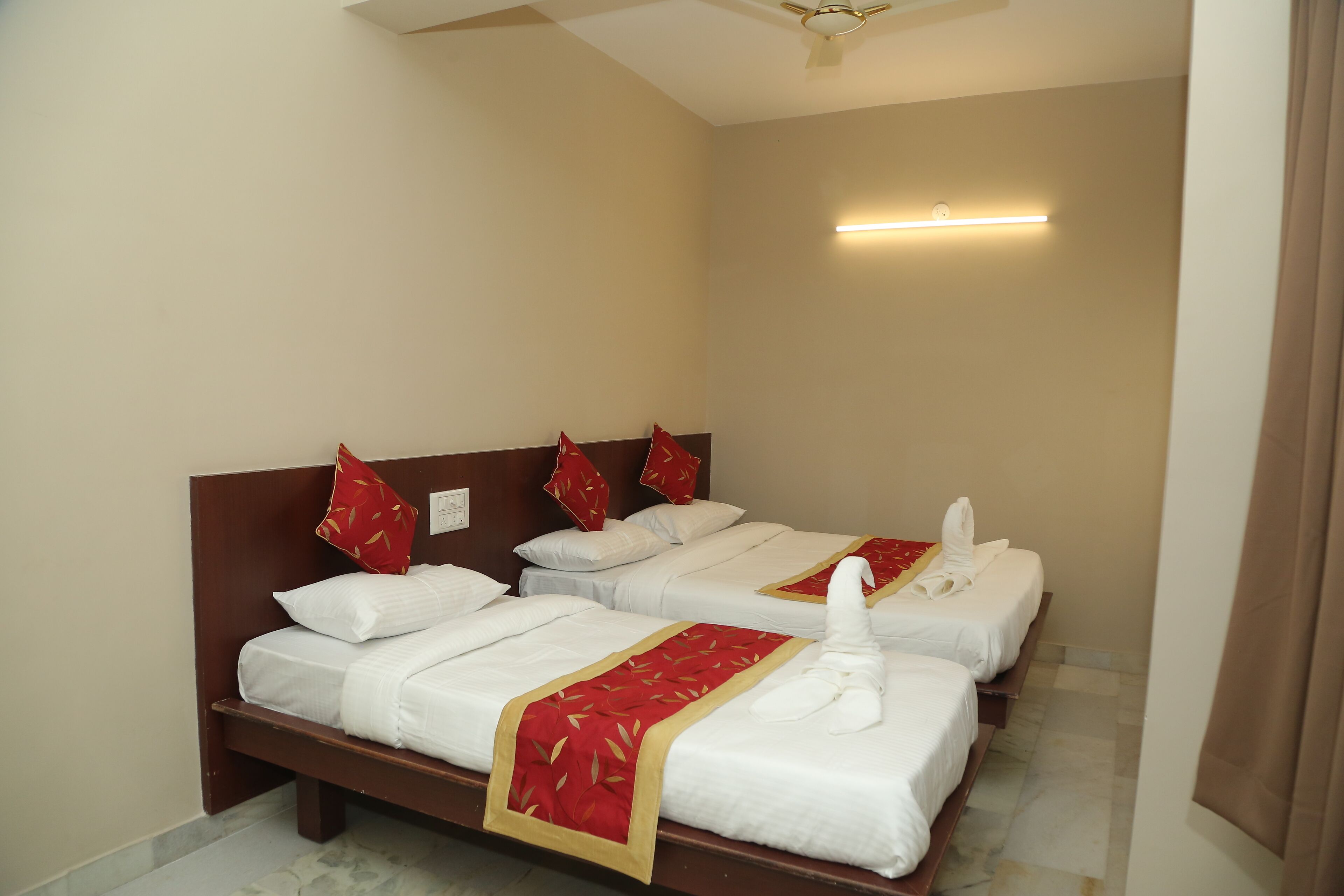 A hotel room with three neatly made beds, each with white linens and red decorative pillows.