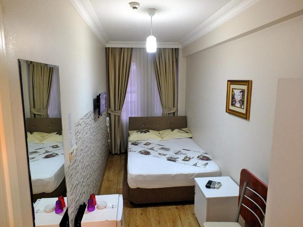 Habitación de hotel con dos camas, una mesita, una silla, un televisor y un cuadro en la pared.