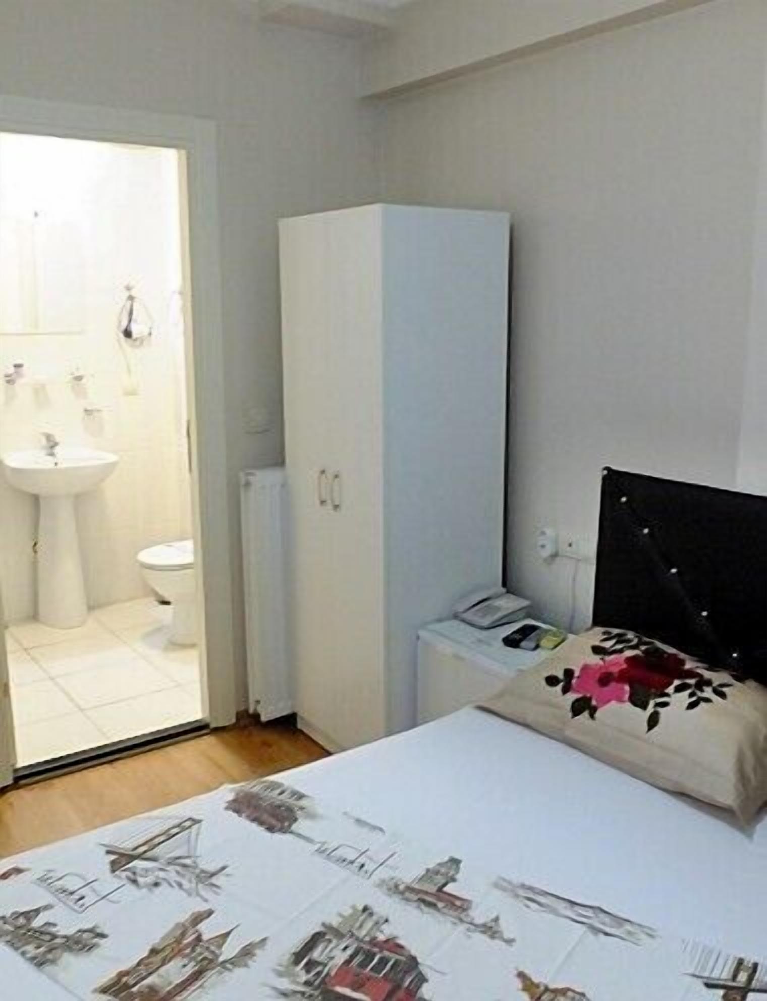 A bedroom with a bed, a wardrobe, a bedside table with a phone, and a bathroom visible through an open door.