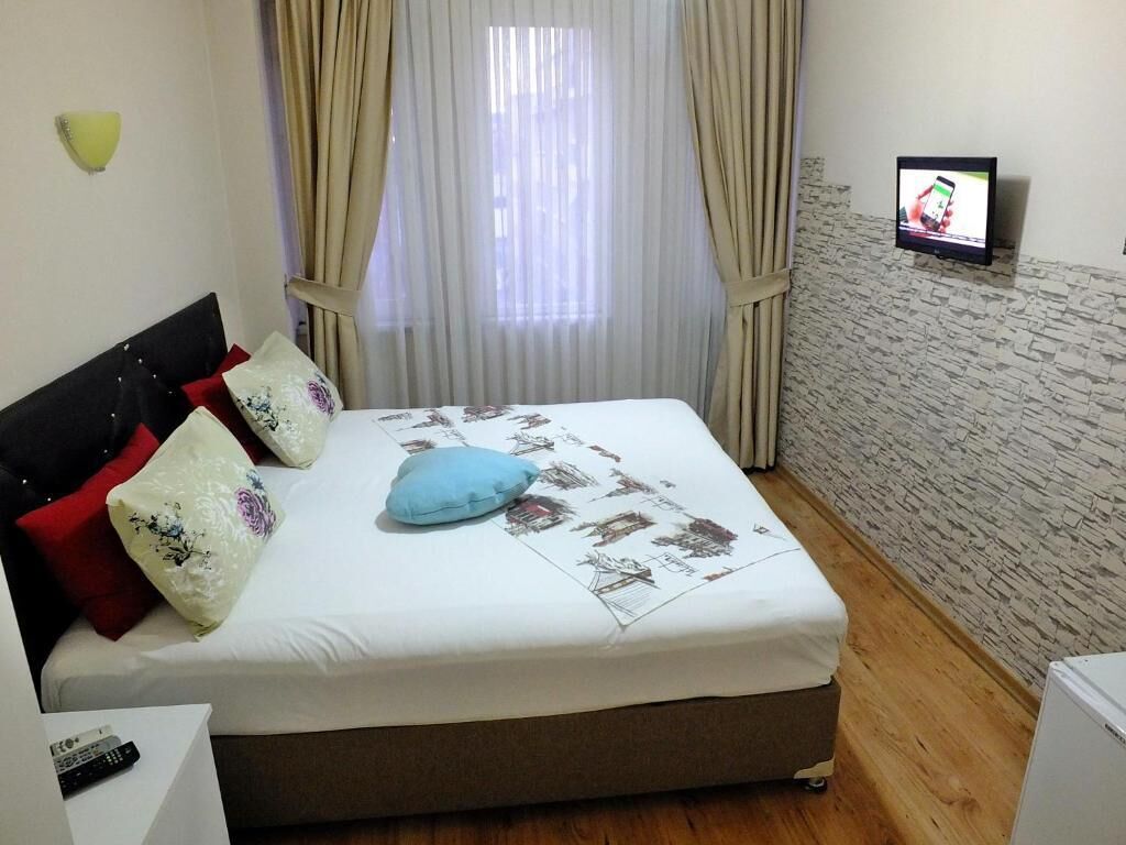 A neatly made bed with a floral-patterned bedspread and several pillows, a television mounted on the wall, and a wooden floor.