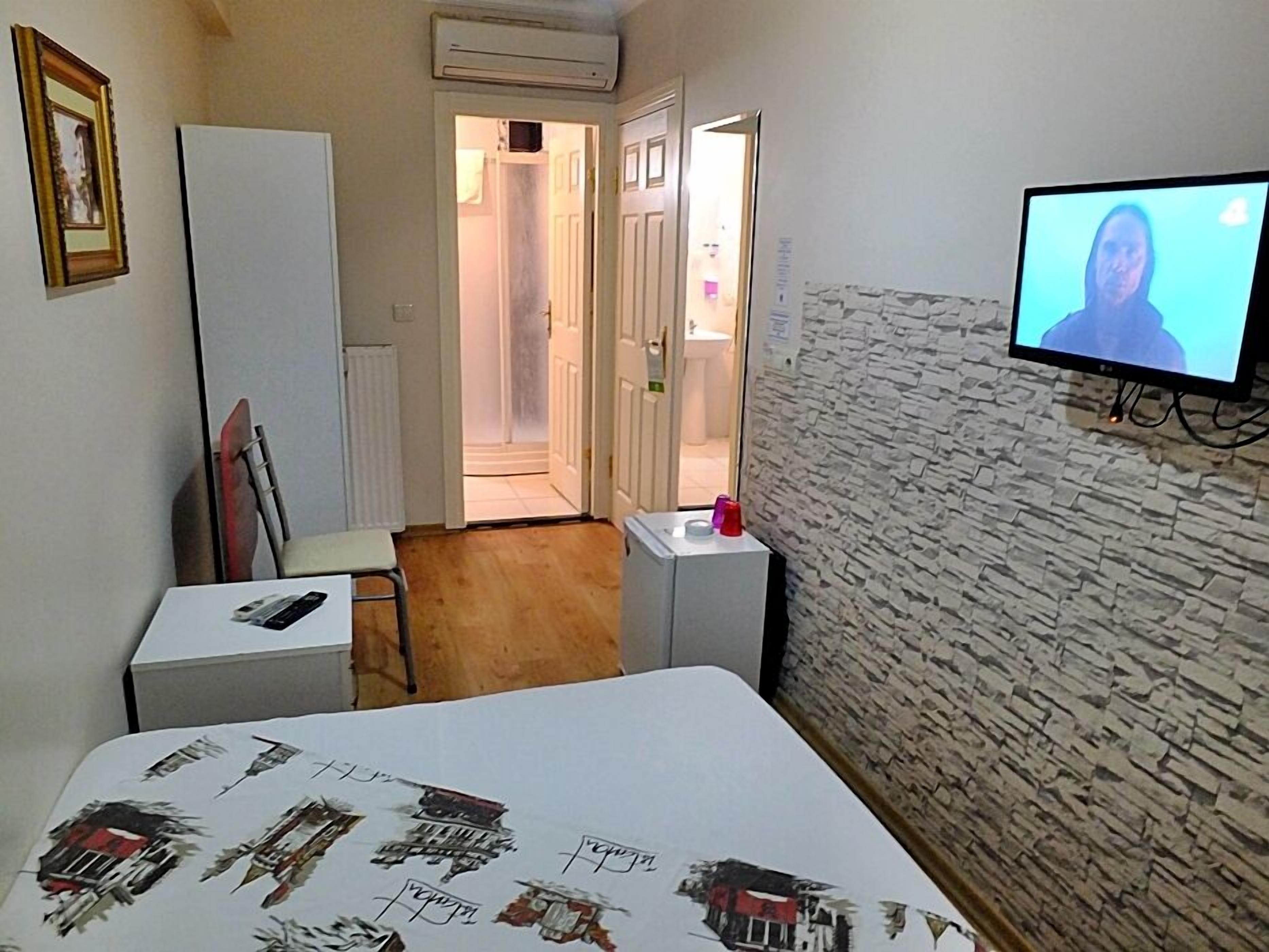 Habitación de hotel con cama, escritorio, silla, televisor y baño visible a través de una puerta abierta.