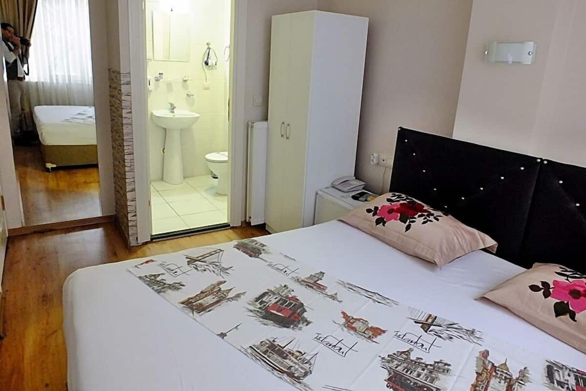 A hotel room with a bed, a nightstand, a wardrobe, a bathroom visible through an open door, and a window with curtains.