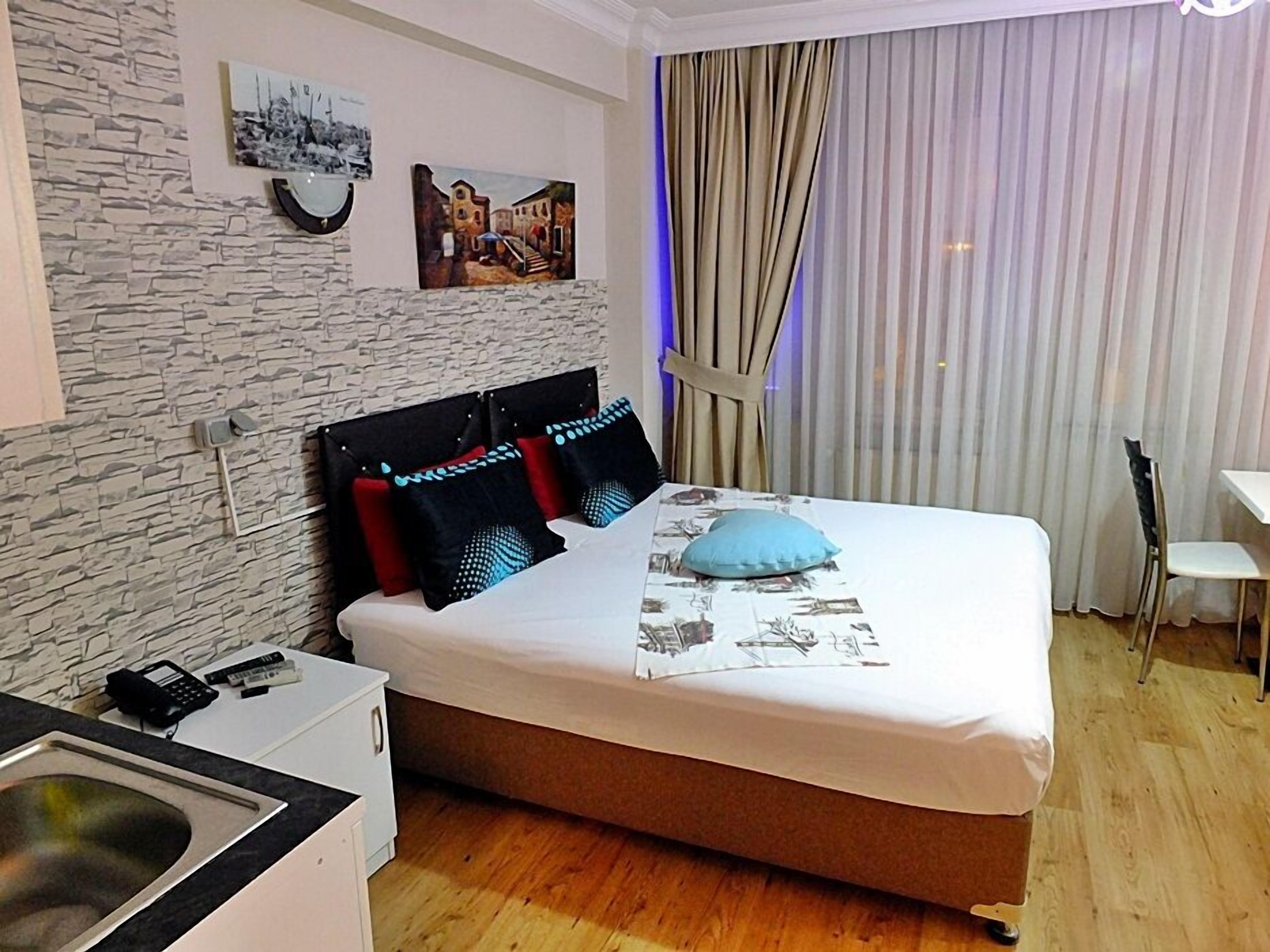 A bedroom with a bed, a small desk, a chair, a sink, and a window with curtains.