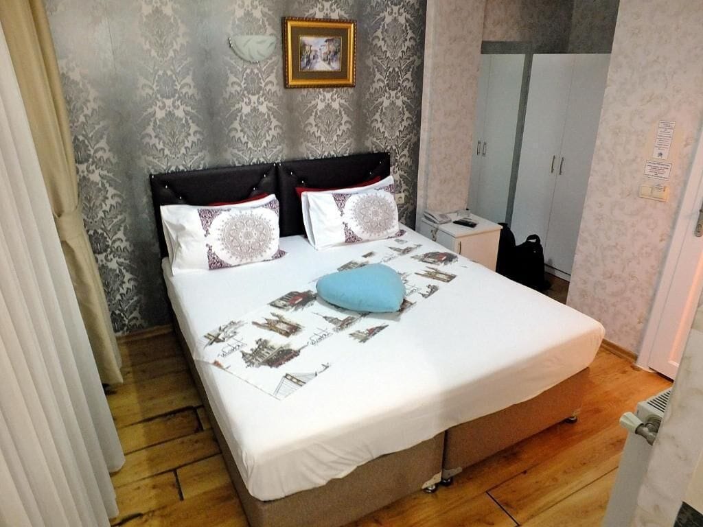 A bedroom with a bed, a nightstand, a wardrobe, and a wall with a framed picture.