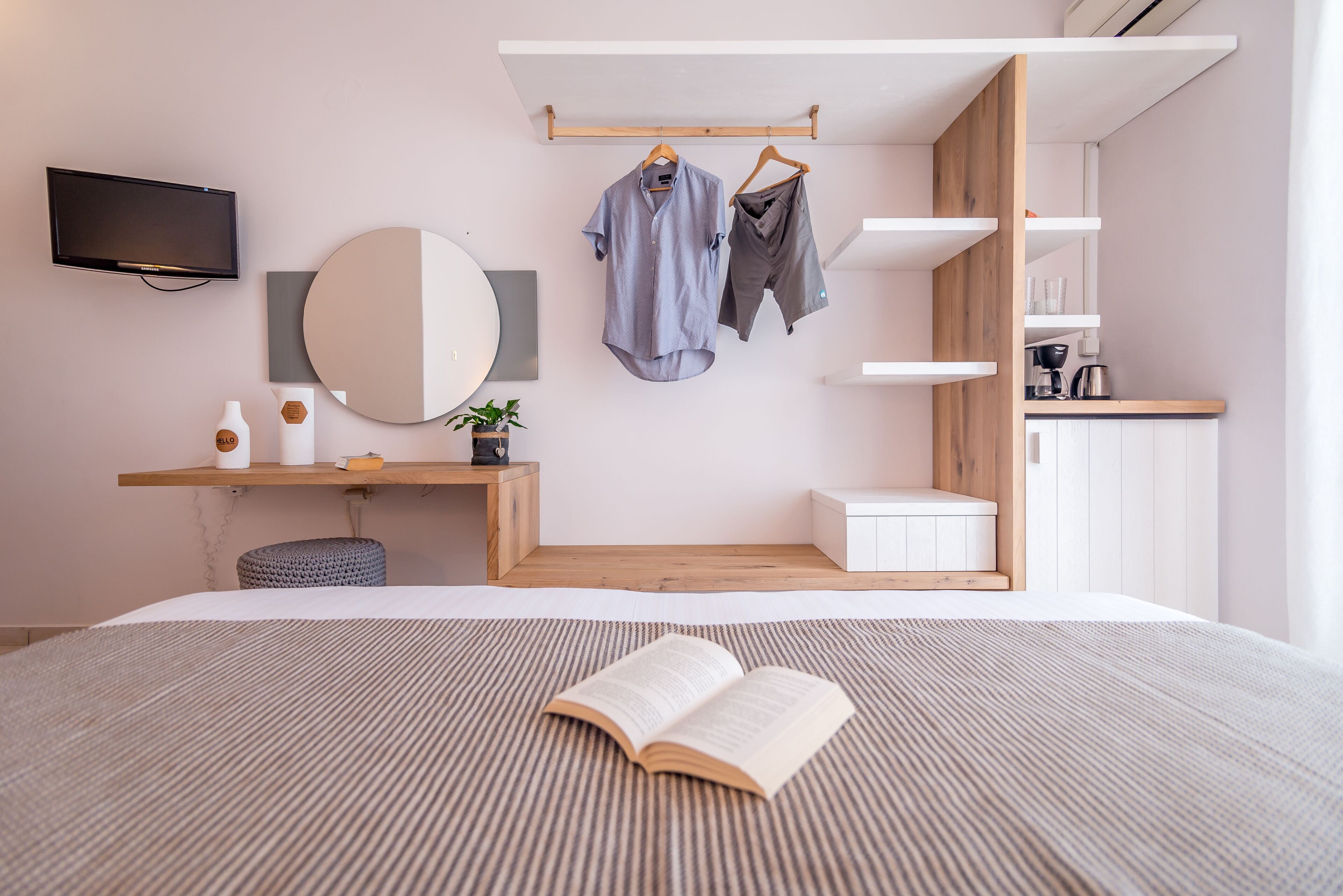 Ein modernes Schlafzimmer mit Bett, Nachttisch mit Spiegel, Fernseher und einer Kleiderstange.