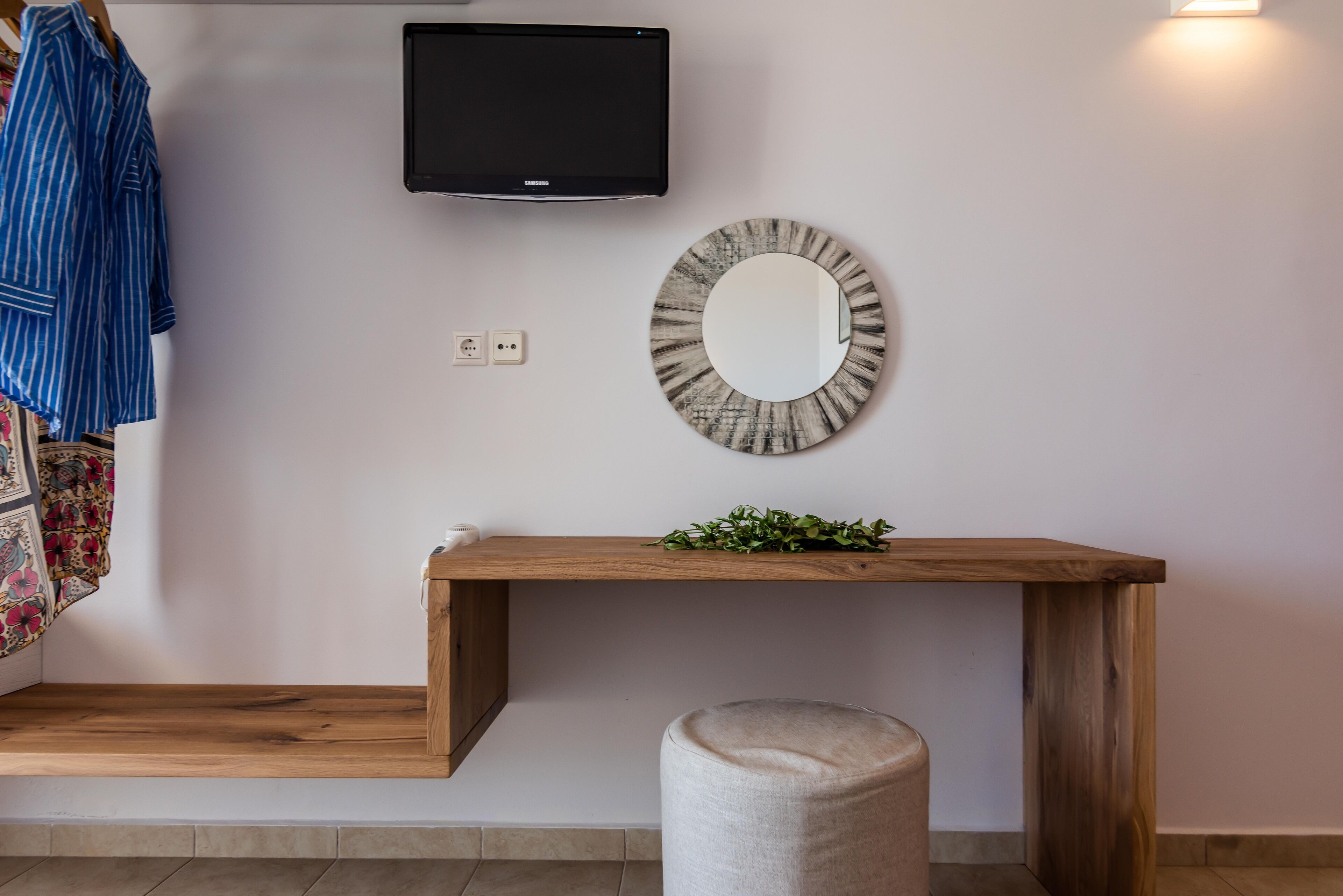 A modern room with a wooden console table, a round mirror, a television mounted on the wall, and a bench.