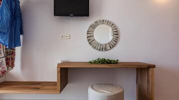 A modern room with a wooden console table, a round mirror, a television mounted on the wall, and a bench.