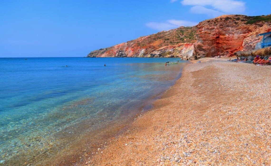 Una playa de guijarros con agua cristalina y un acantilado rocoso.