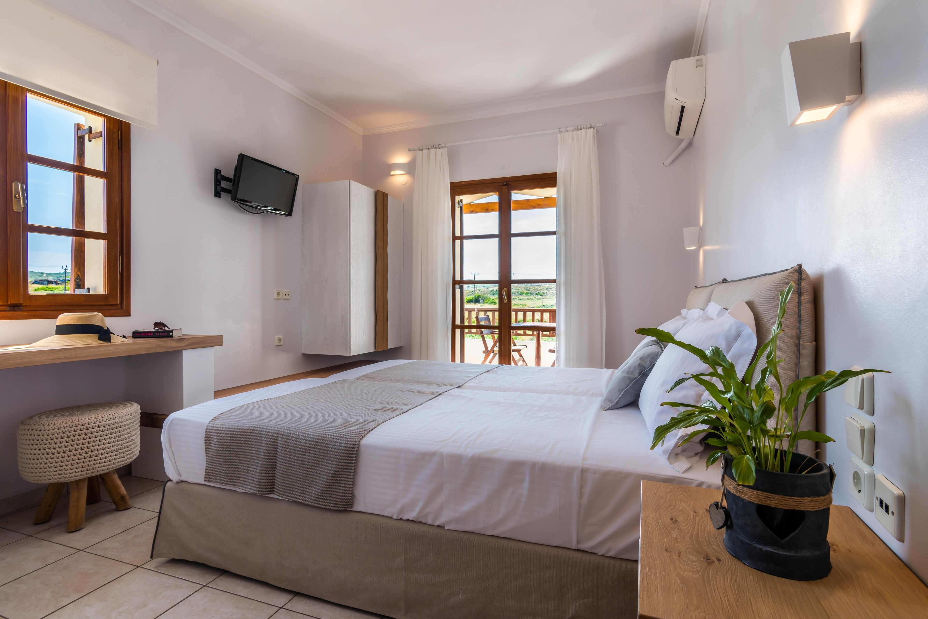 A bedroom with a bed, a bedside table, a TV, a window, and a view of the outdoors.