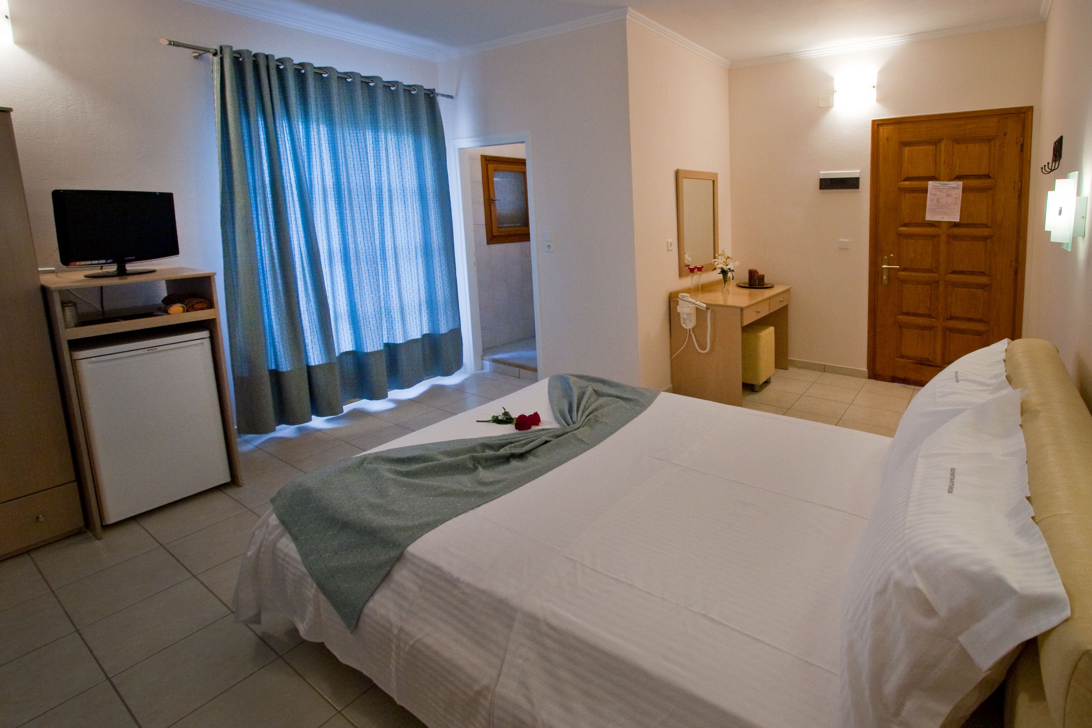 Una habitación de hotel con una cama, un escritorio con una computadora, un baño y una puerta.