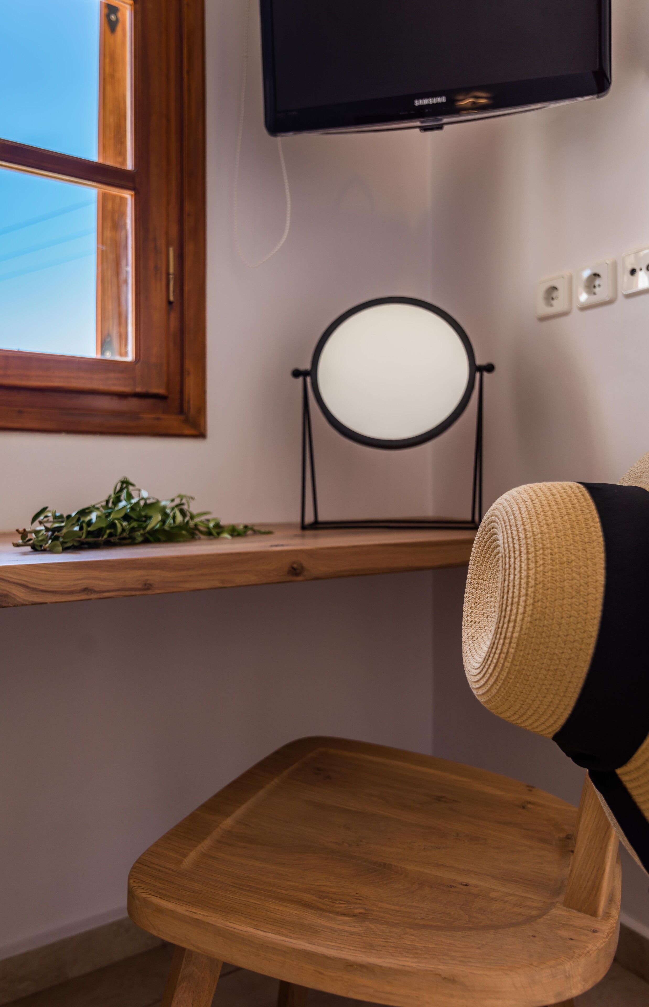 A wooden desk with a mirror, a television mounted above, and a chair with a woven backrest.
