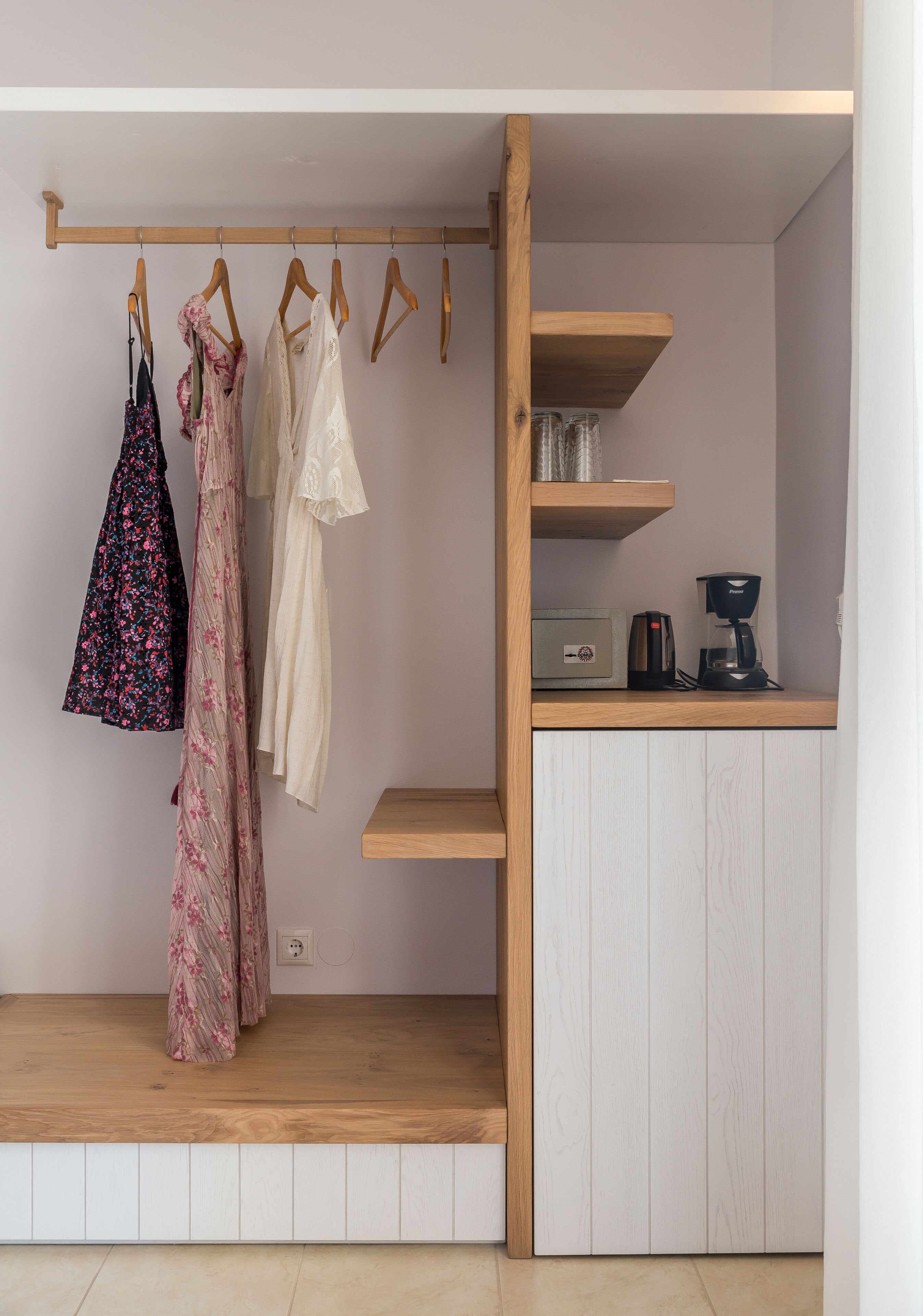 Habitación pequeña con un armario de madera, una percha para ropa y una cafetera sobre una estantería.