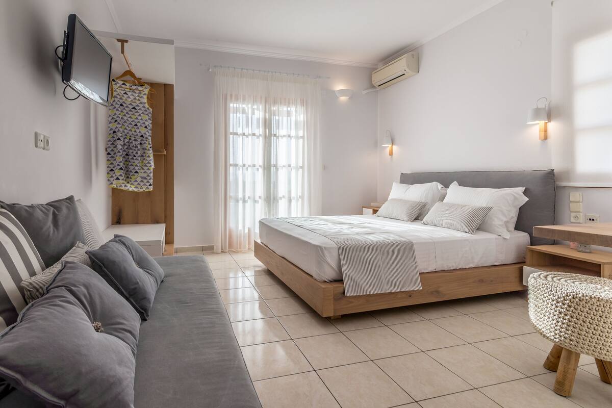 A modern bedroom with a bed, a sofa, a TV, and a window with curtains.