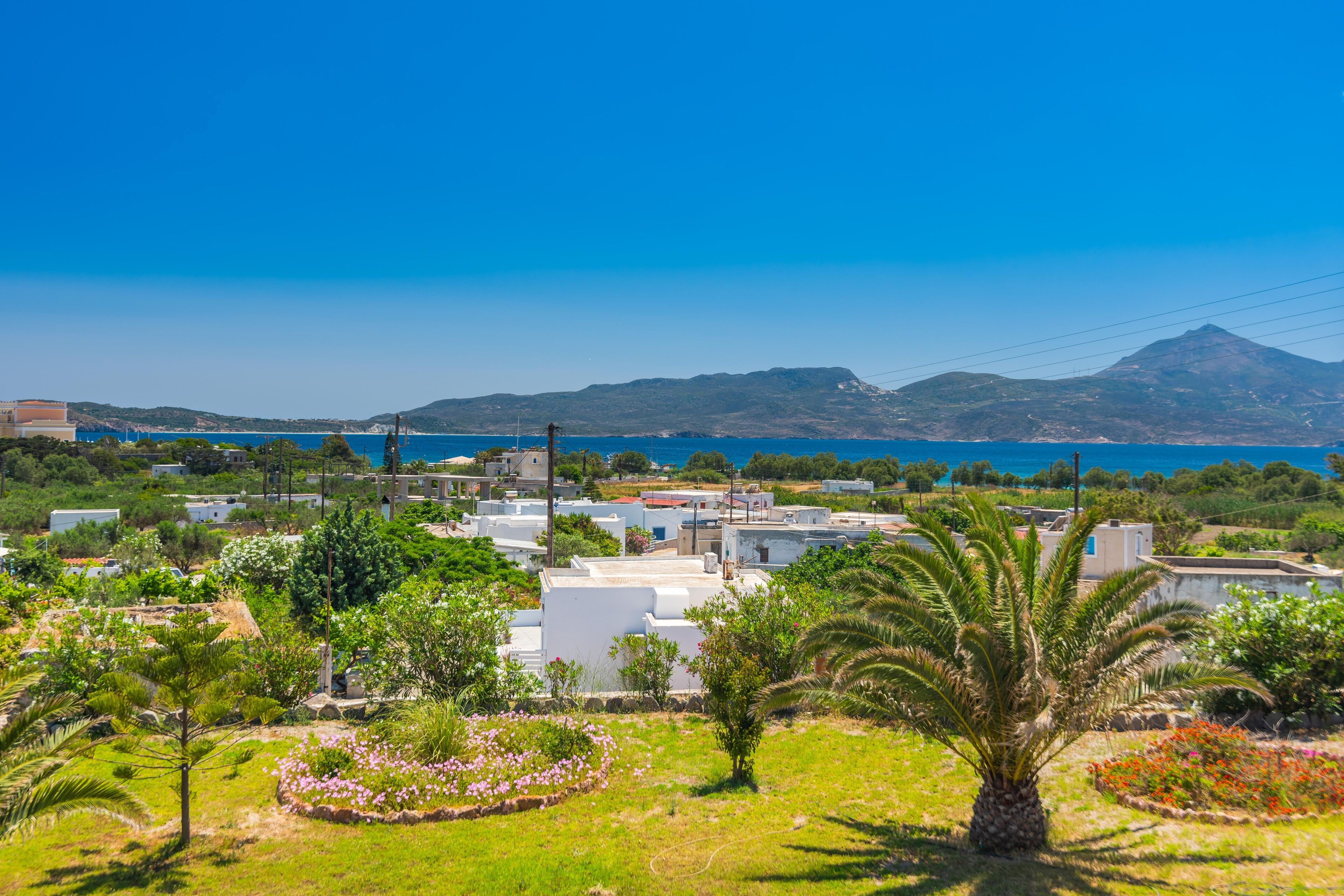 A coastal village with white buildings, green landscapes, and a mountain in the background.