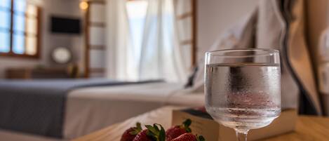 A room with a bed, a bedside table with a glass of water and strawberries, and a TV on the wall.