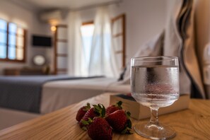 A room with a bed, a bedside table with a glass of water and strawberries, and a TV on the wall. - Konstantinos (Milos)
