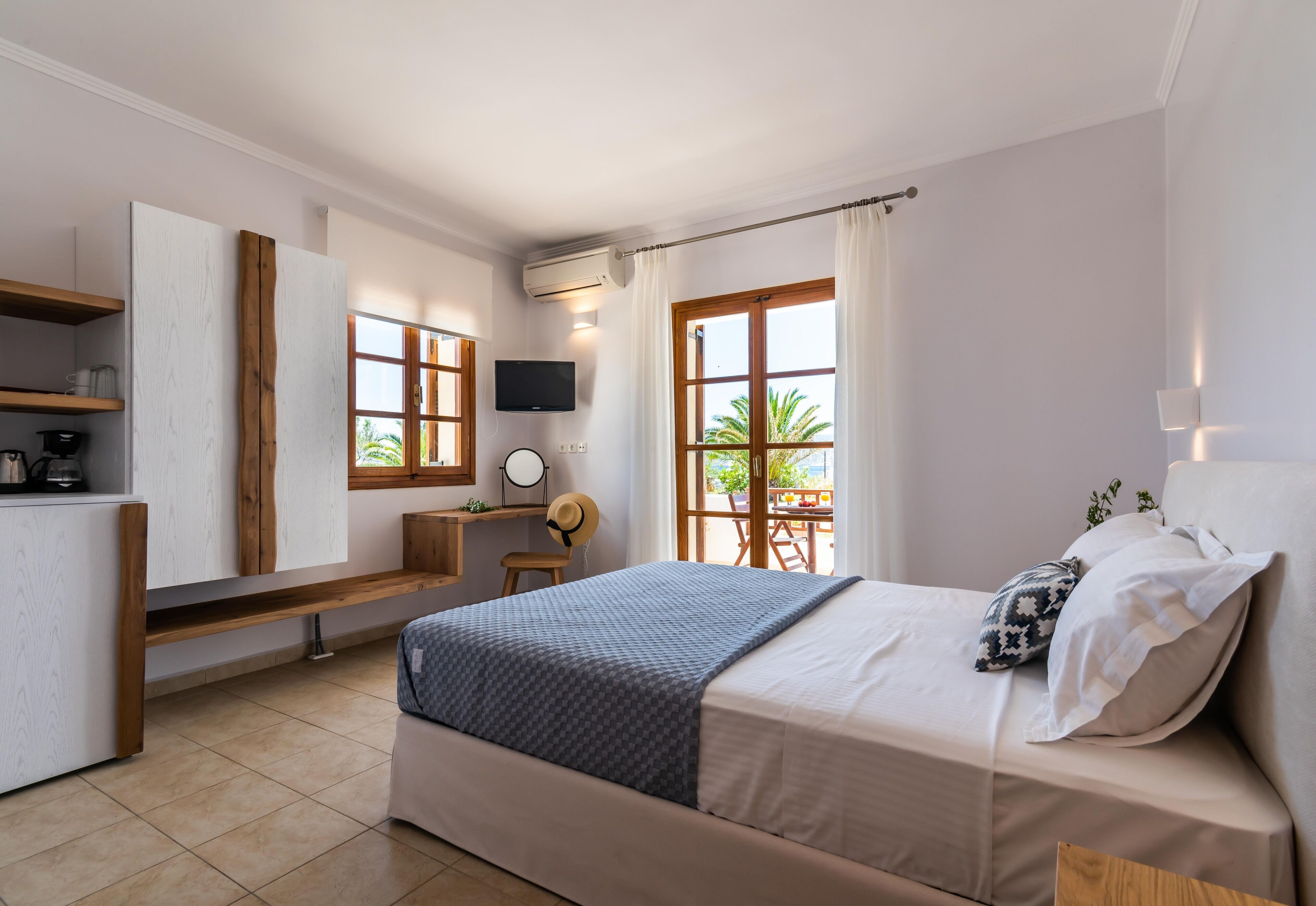 A bedroom with a bed, a desk, a TV, and a balcony with a table and chairs.