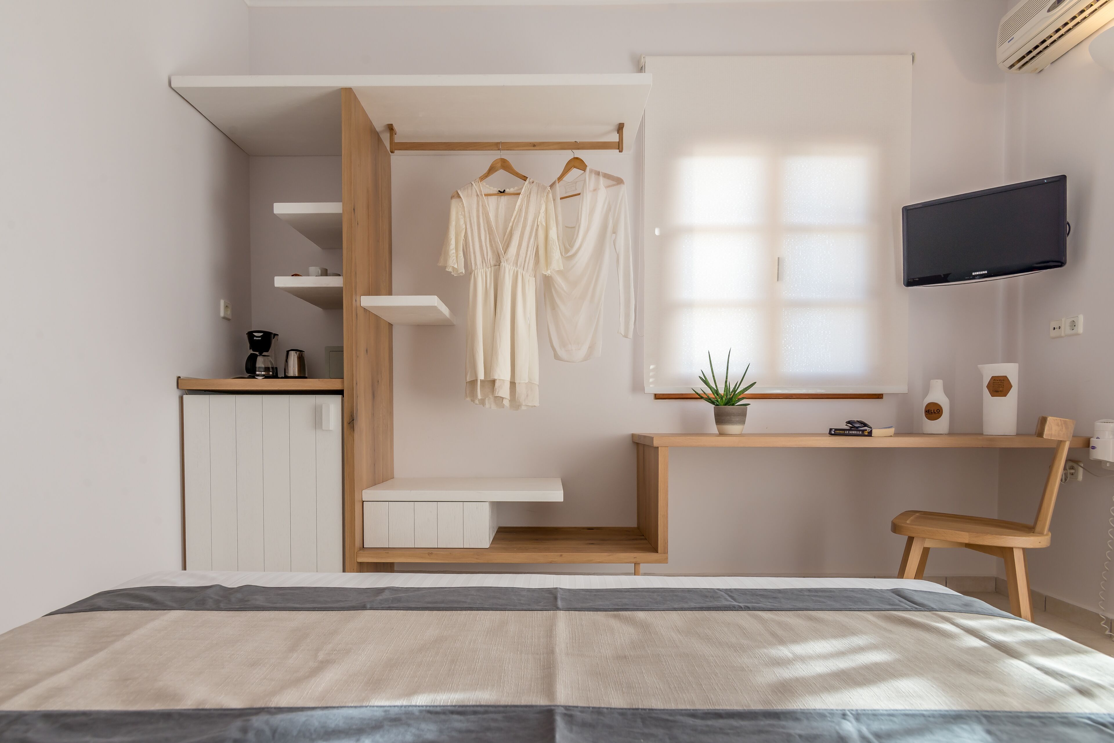 Une chambre à coucher avec un lit, un bureau, une chaise, une télévision et une armoire où sont suspendus des vêtements.