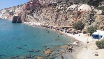 Una playa con agua turquesa cristalina, afloramientos rocosos y montañas al fondo.