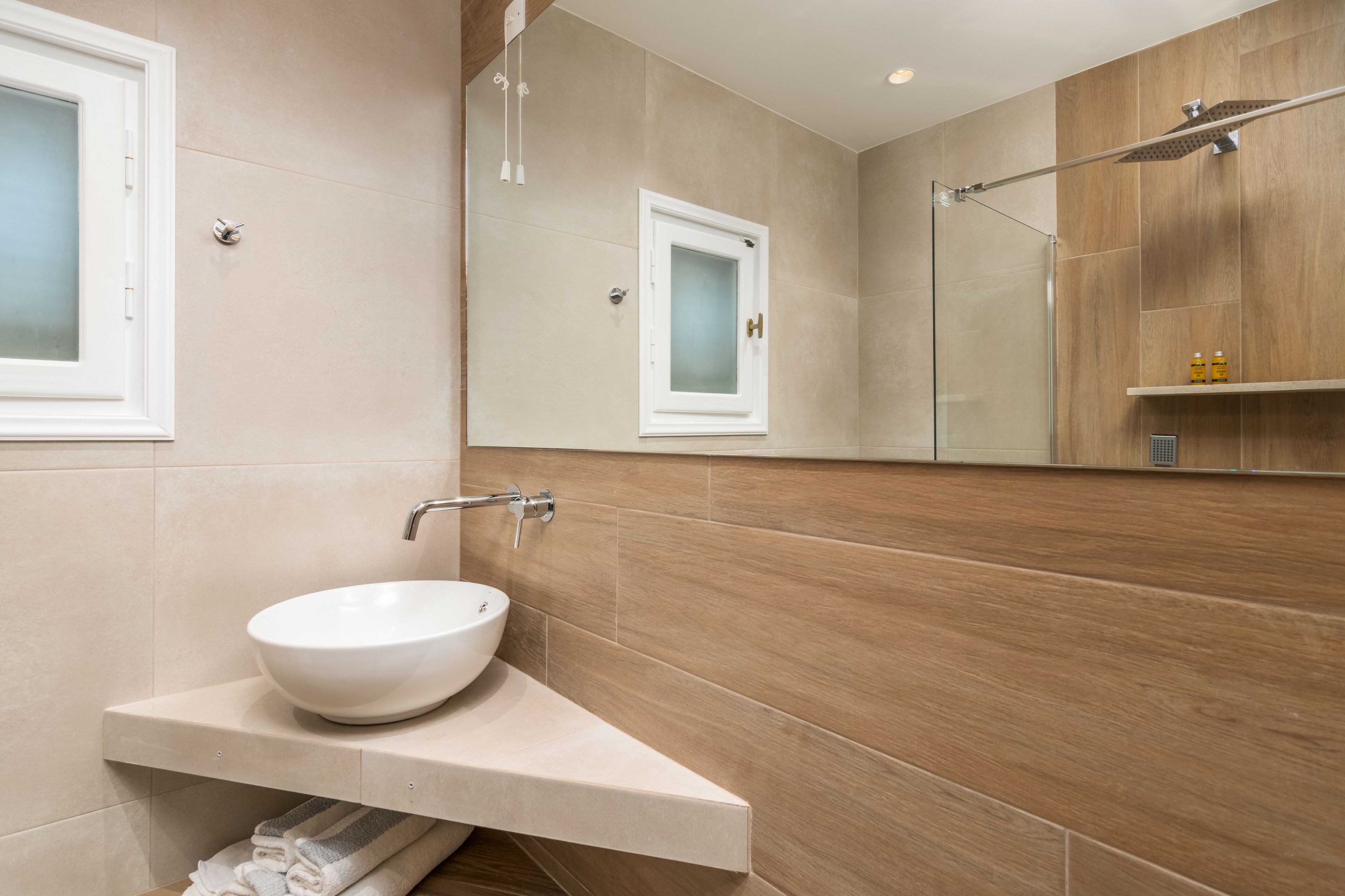 Un baño moderno con un lavamanos blanco tipo recipiente, una cabina de ducha con paredes de vidrio y un mueble de tocador de madera.