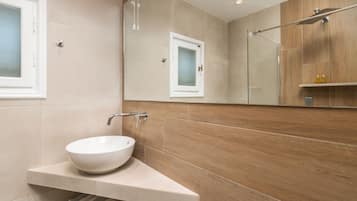 Un baño moderno con un lavamanos blanco tipo recipiente, una cabina de ducha con paredes de vidrio y un mueble de tocador de madera.