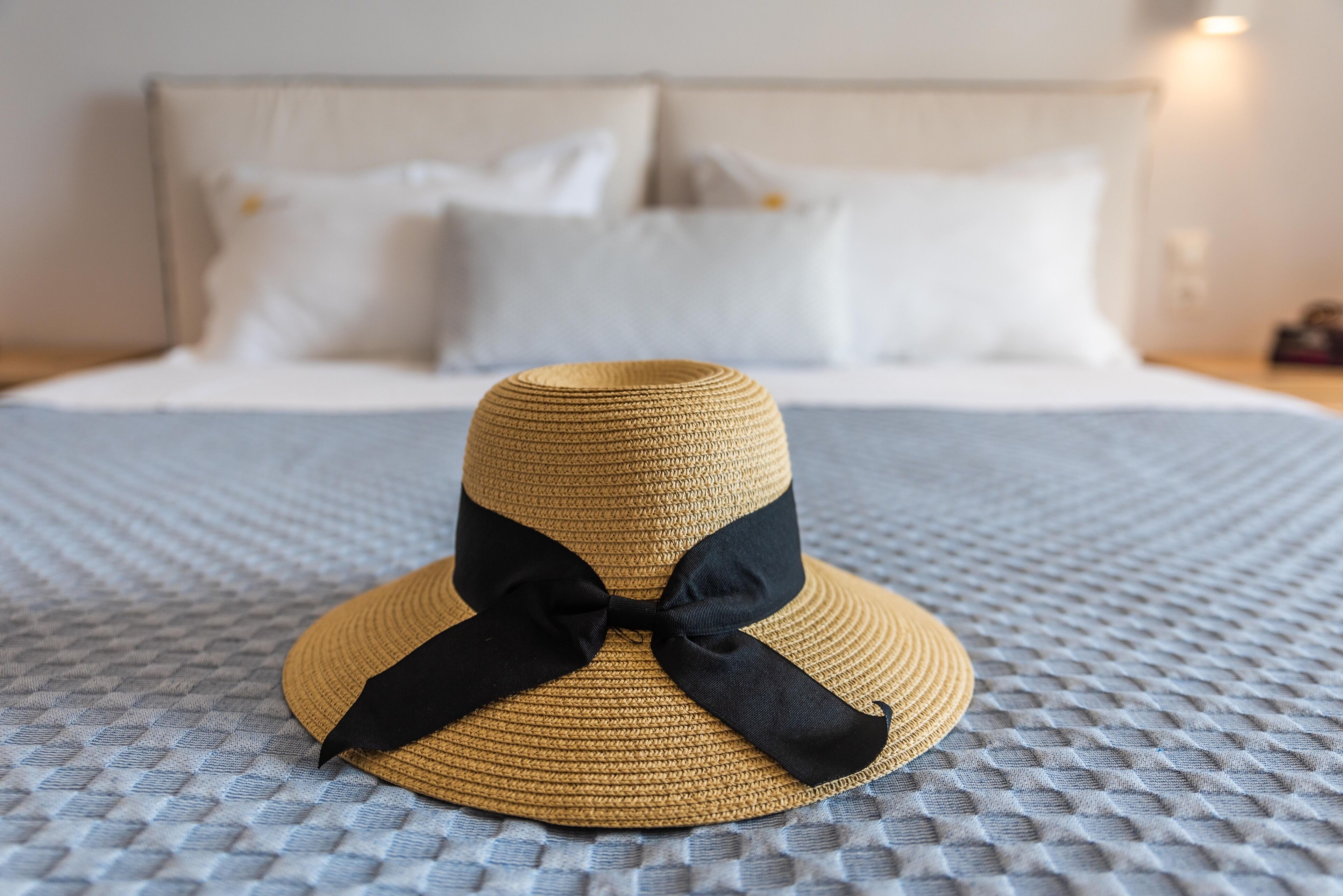 Un sombrero de paja con un lazo negro sobre un edredón con textura.