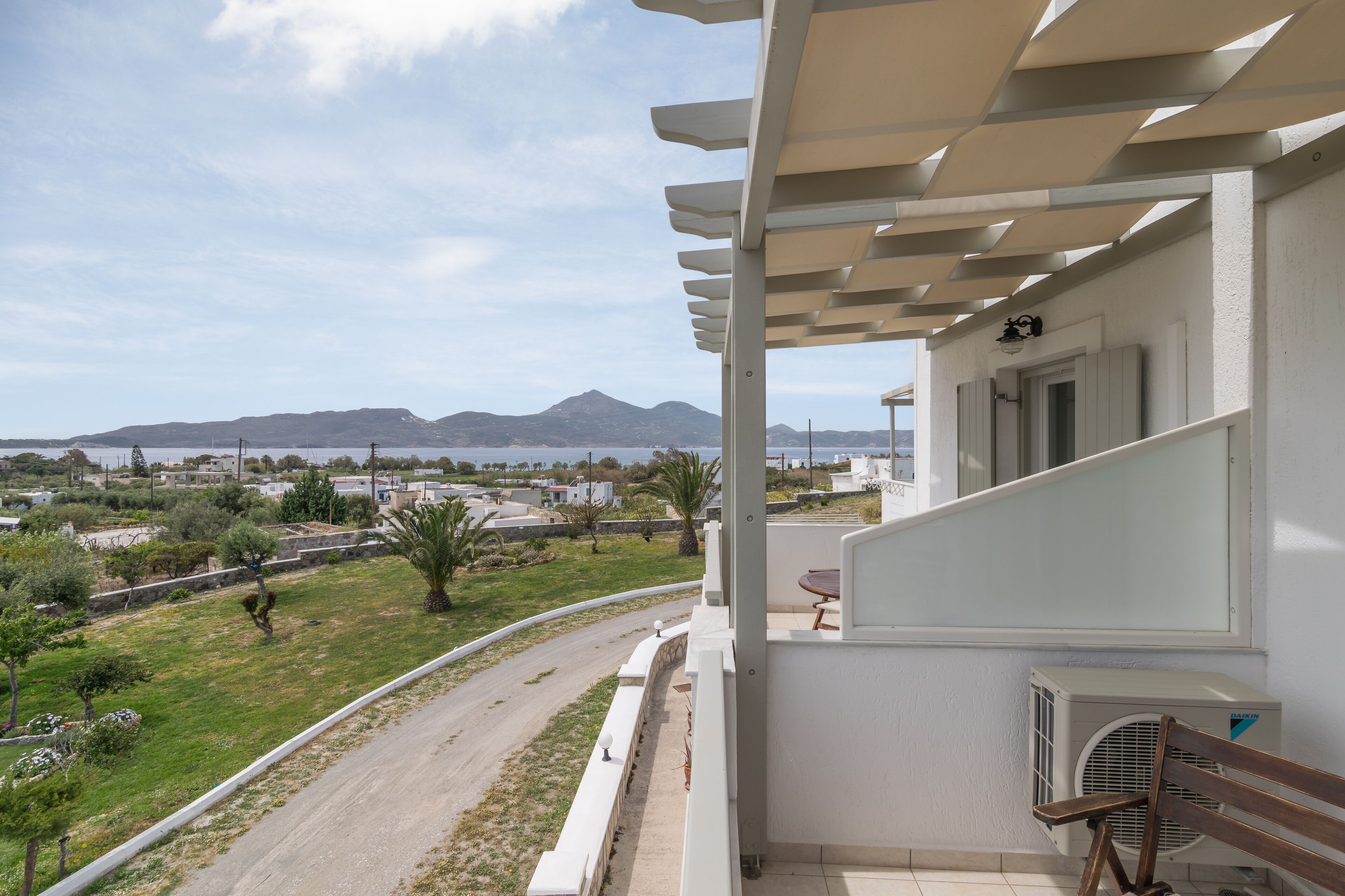 A balcony with a view of a road and distant mountains, a bench, and an air conditioning unit.