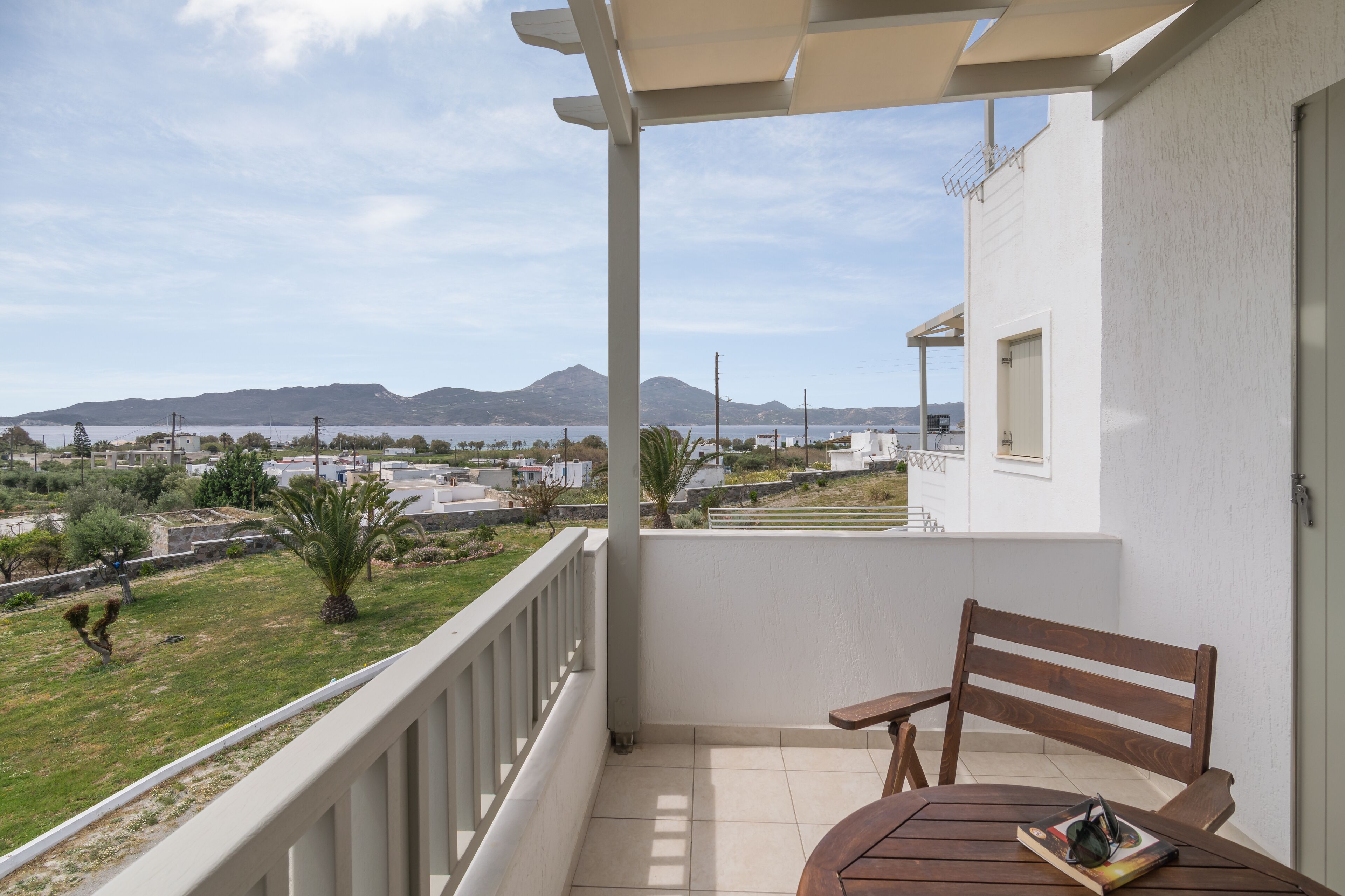 A balcony with a wooden table and chair, overlooking a grassy area with a mountain in the distance.