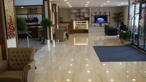 Um hall de hotel com piso de mármore, balcão de recepção, televisão e áreas de estar.