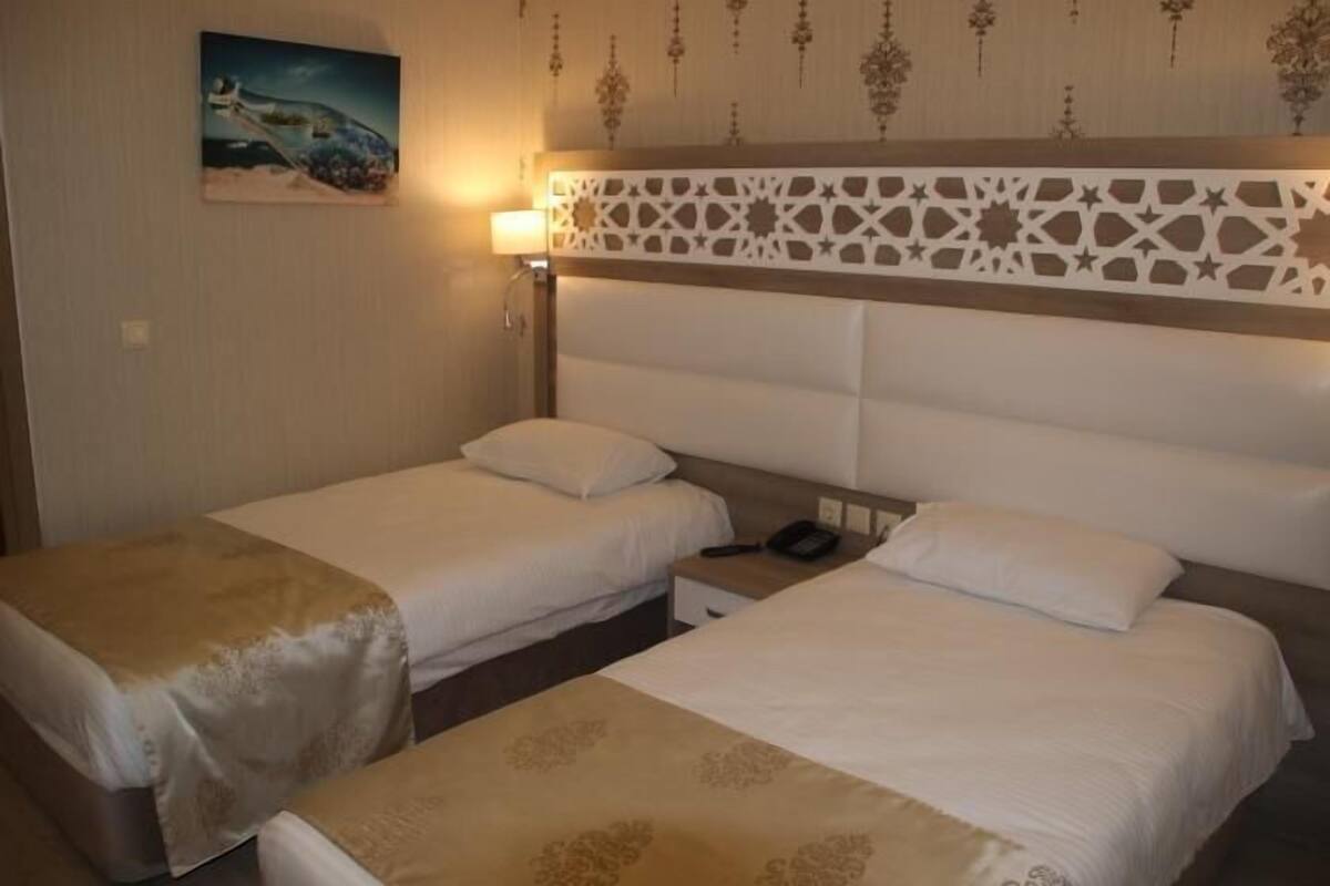 Een hotelkamer met twee eenpersoonsbedden, een nachtkastje met een telefoon, een wandlamp en een decoratief hoofdeinde.