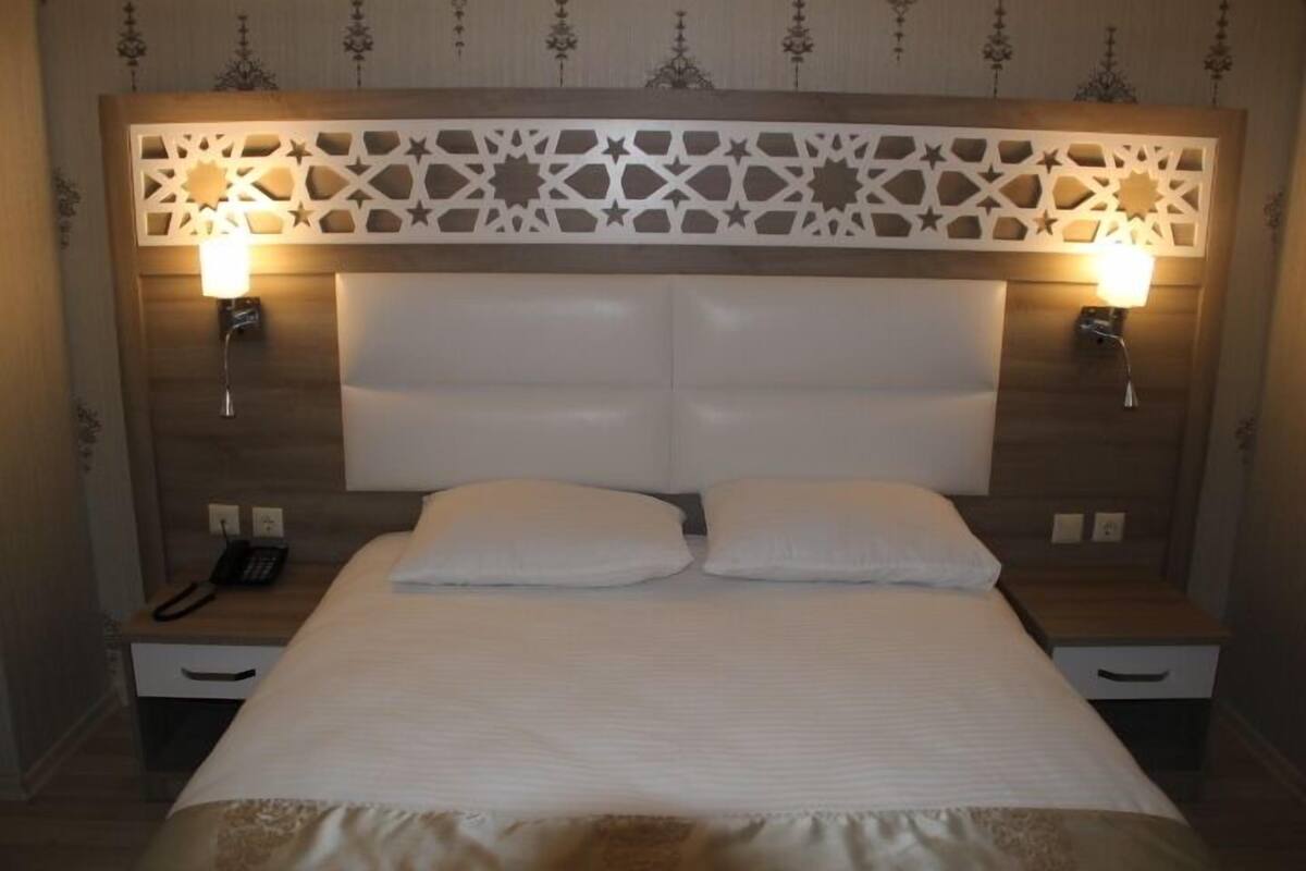 Hotelkamer met een groot bed, twee nachtkastjes, een decoratief hoofdeinde en wandlampen.