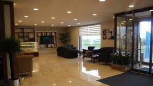 Um hall amplo com piso de mármore polido, área de estar com sofás, televisão e uma grande janela com persianas.