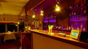 Zona de bar con estanterías de madera llenas de botellas, un menú en la pizarra y luces colgantes.